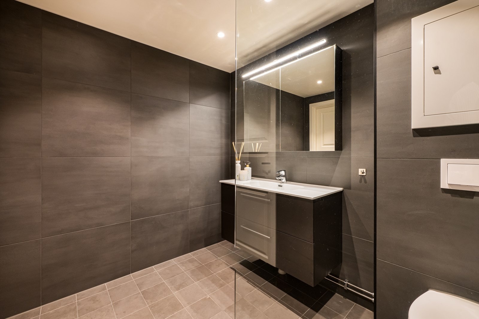 Rommet er innredet med servantskap med heldekkende servant, speilskap med integrert belysning, vegghengt toalett og dusjhjørne med glassfelt, regnfallsdusj og hånddusj. Galleribilde