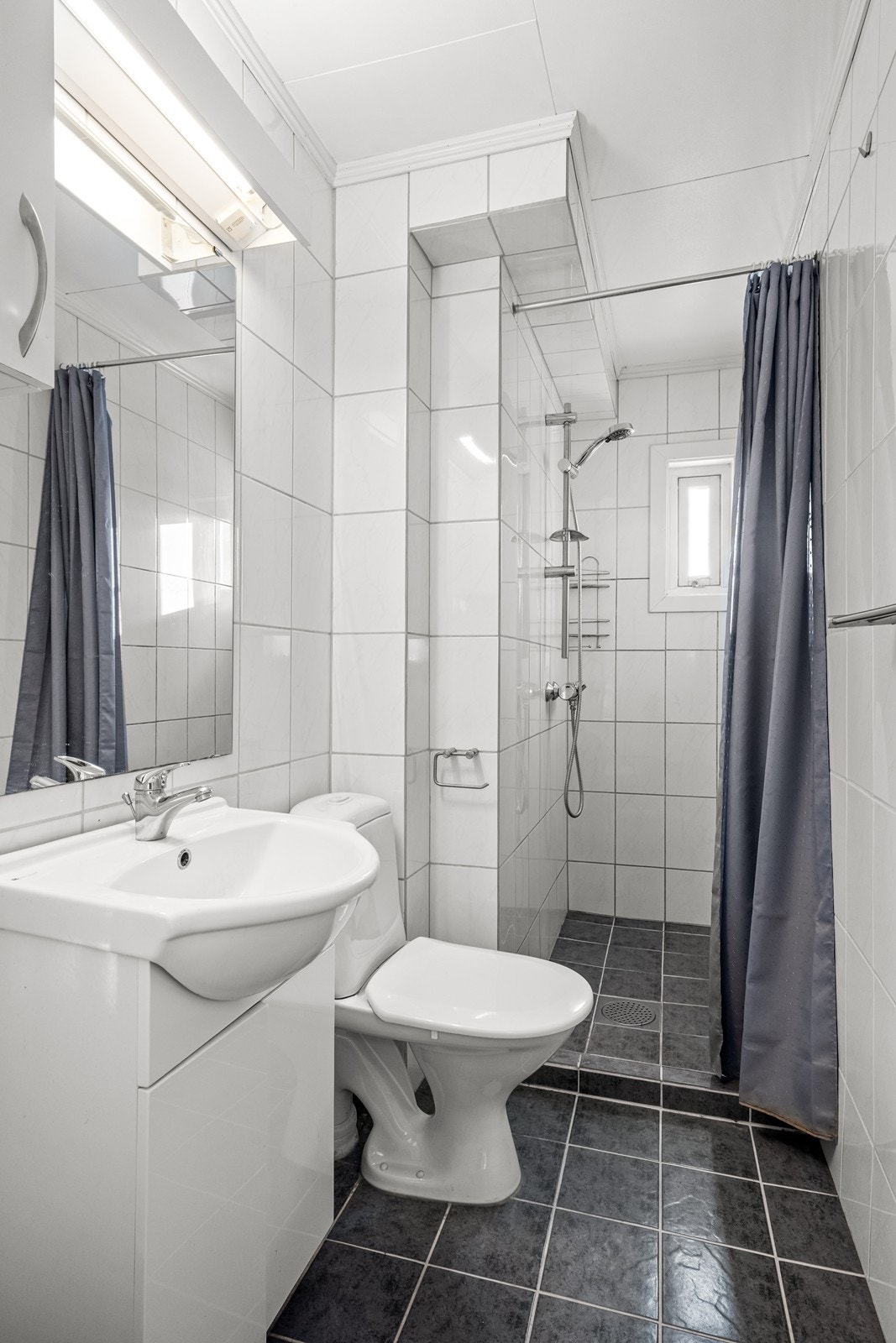 Badet er flislagt og utstyrt med servant med underskap og et dusjhjørne. Galleribilde