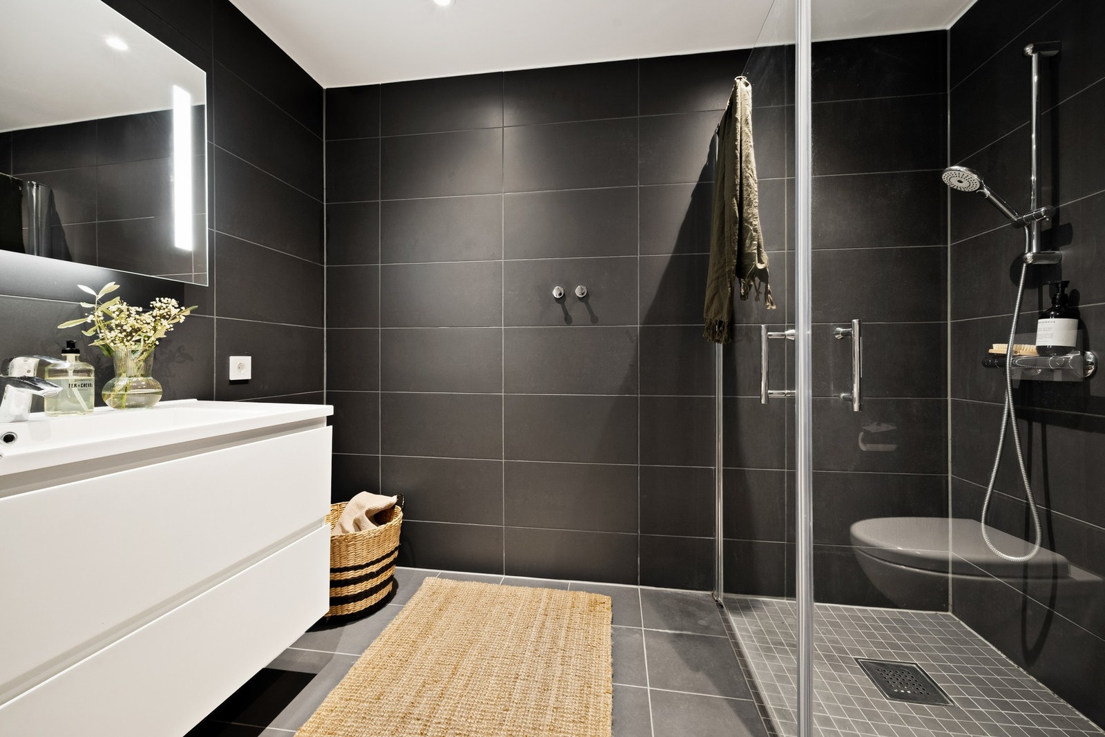 Delikat flislagt bad med smakfulle materialvalg. Vegghengt speilskap, heldekkende servant over skuffer Galleribilde