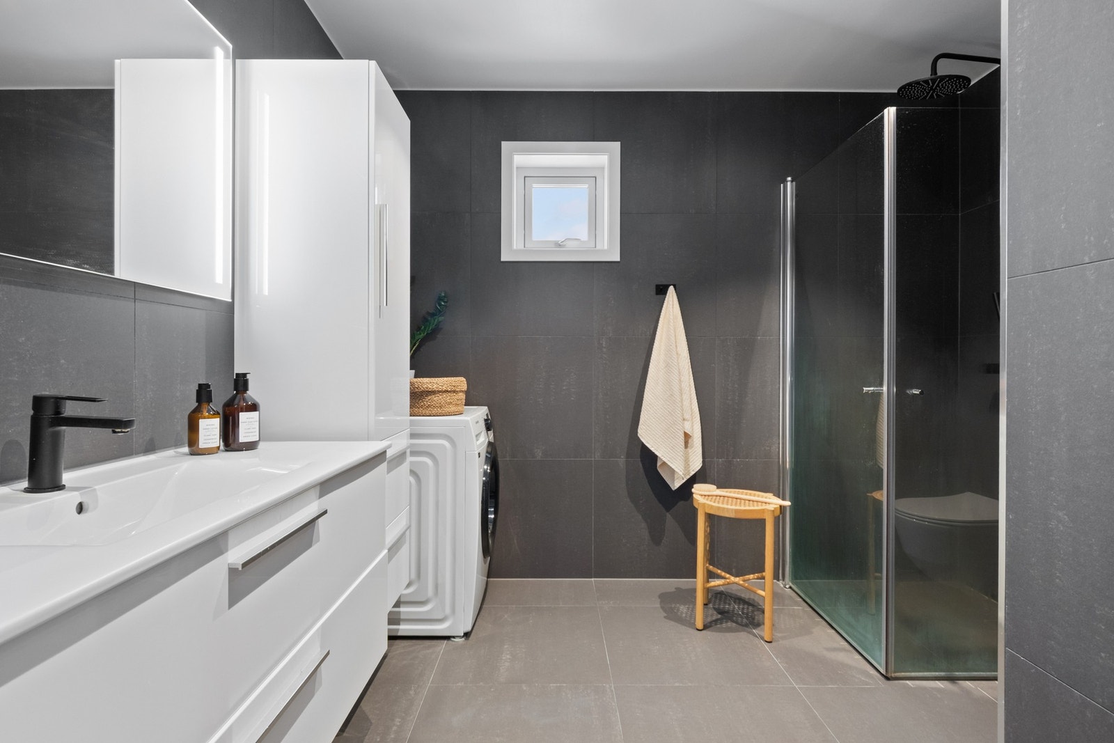 Badet fremstår som romslig og delikat, med store koksgrå fliser på veggene og lysegrå gulvfliser med gulvvarme. Galleribilde