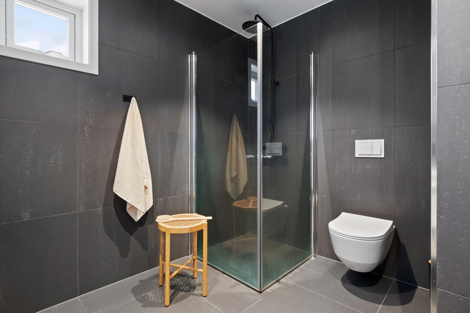 Badet er utstyrt med vegghengt toalett, opplegg for vaskemaskin og dusjhjørne med regnfallsdusj og innfellbare glassdører. Galleribilde