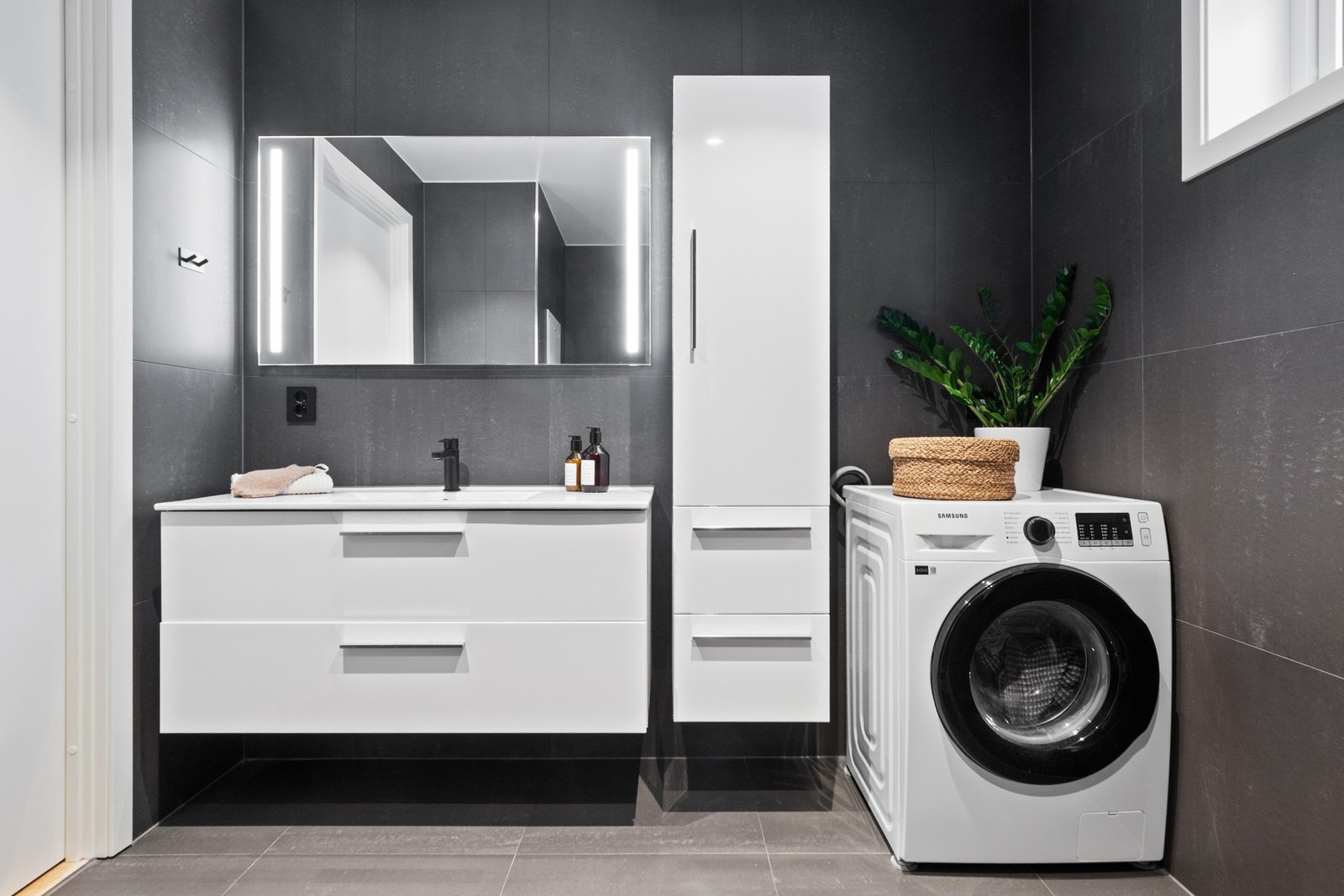 Baderomsinnredningen har hvite fronter og består av en heldekkende servant på en skuffeseksjon, et høyskap og et speil med integrert belysning. Galleribilde