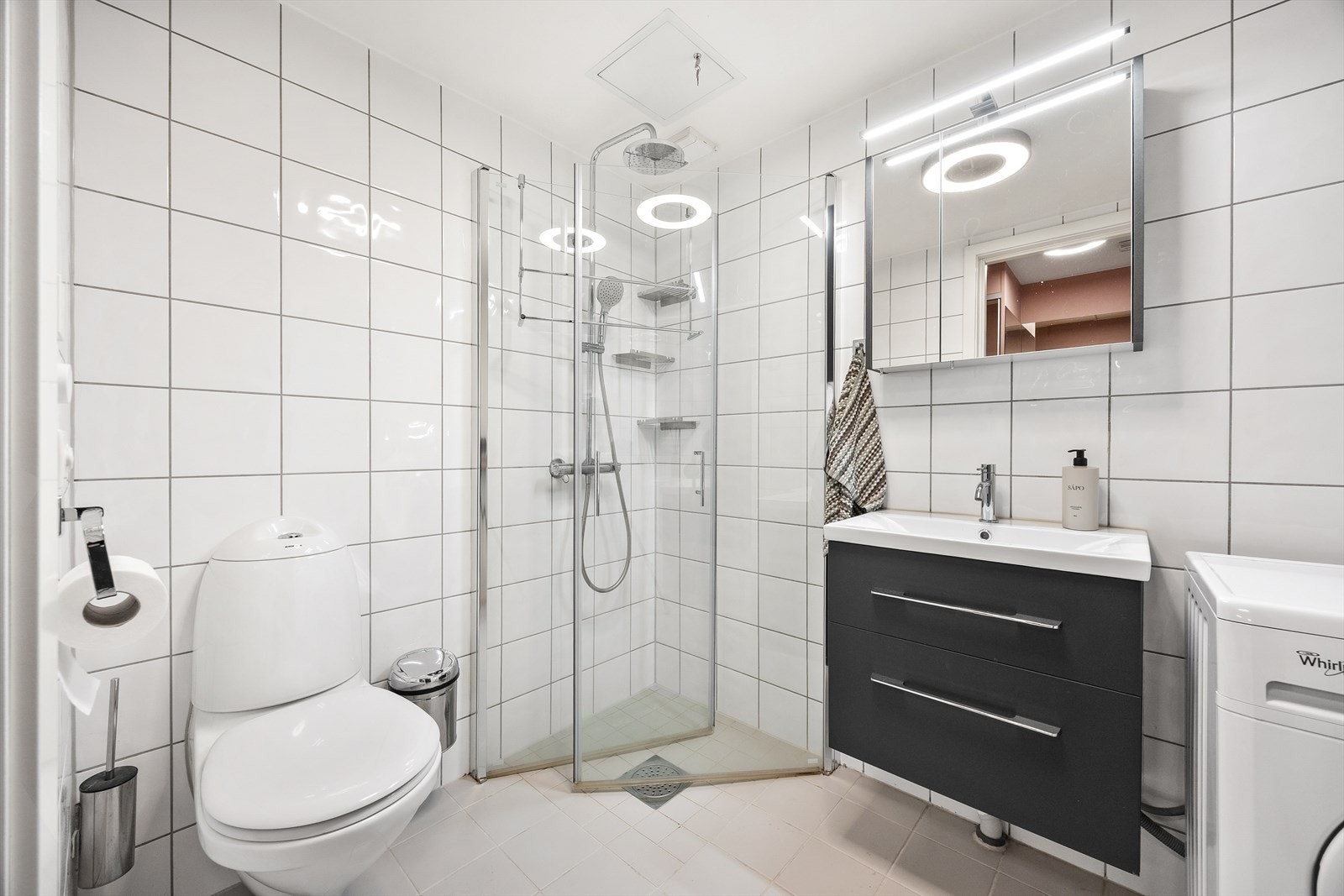 Badet inneholder vegghengt toalett og et dusjhjørne med innfellbare glassdører. Galleribilde