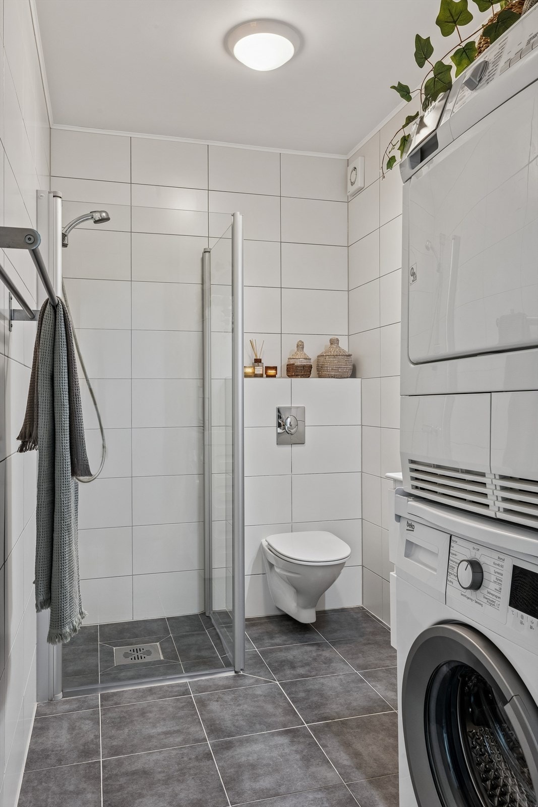 Flislagt bad med vegghengt toalett og dusjhjørne med innfellbare glassdører. Galleribilde