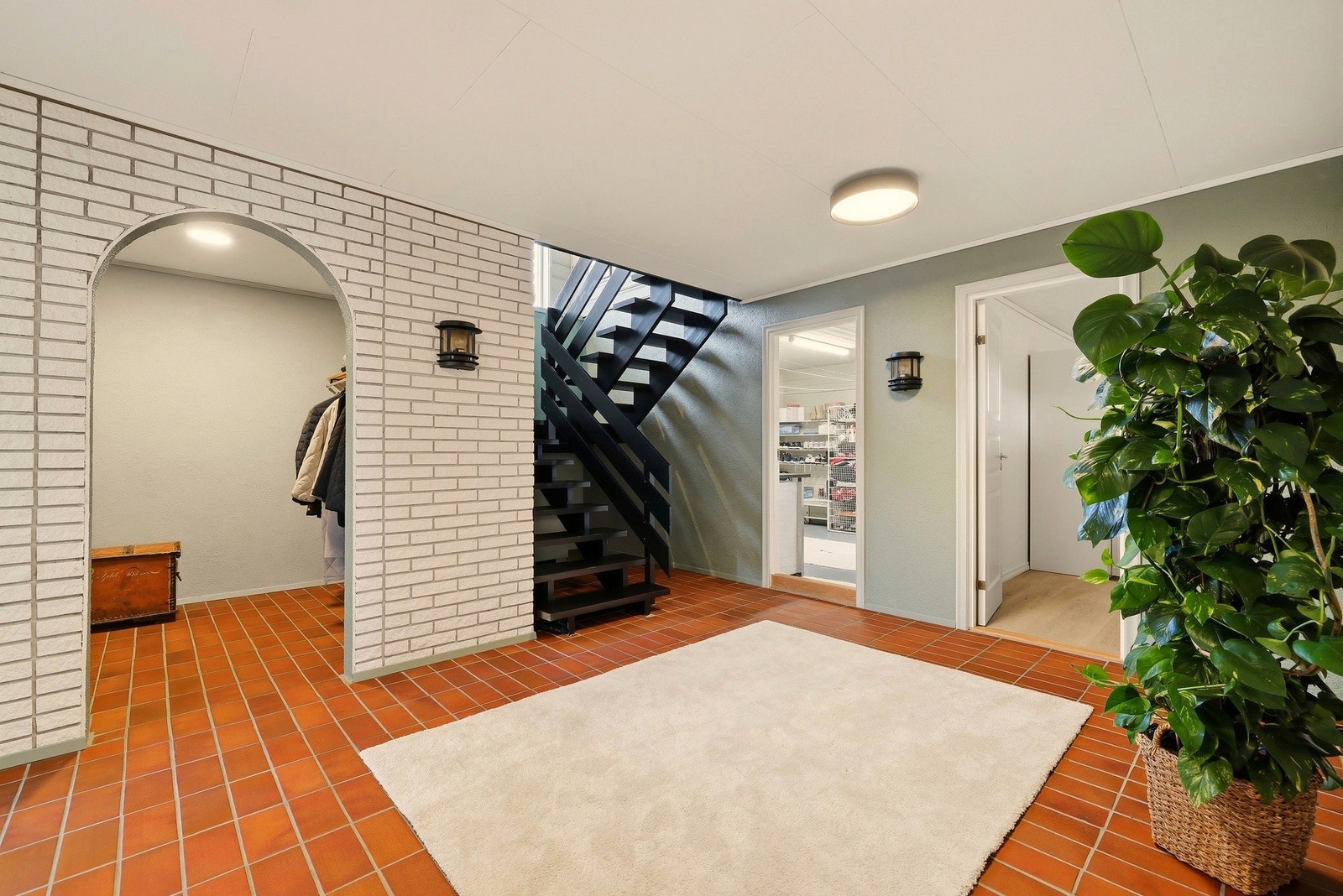 Romslig hall med flislagt gulv og interntrapp til hovedplanet over. Galleribilde