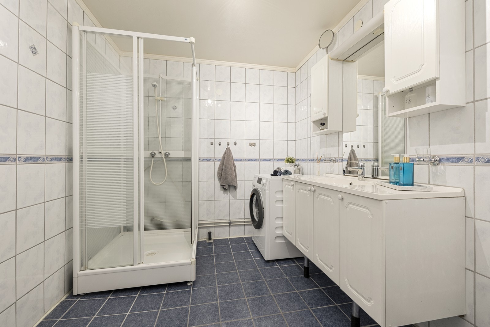 Flislagt baderom med dusjkabinett, servantinnredning og opplegg for vaskemaskin. Galleribilde
