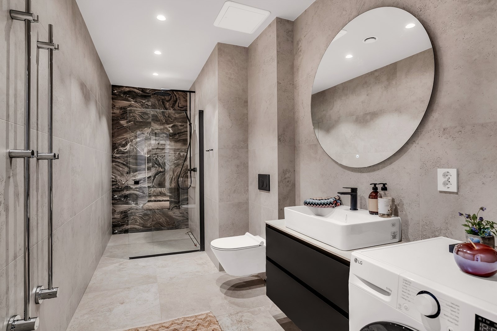 Delikat bad med tidsriktige fliser og varme i gulv. Badet er innredet med veggmontert toalett, opplegg for vaskemaskin og tørketrommel, dusjdører i herdet glass, veggspeil med integrert belysning Galleribilde