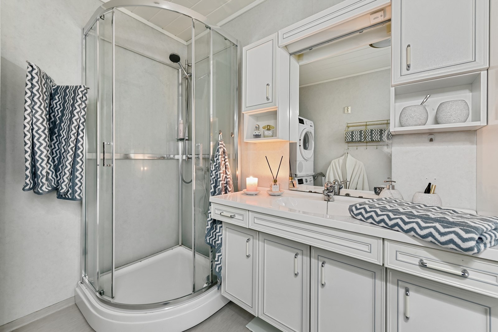 Innredningen inkluderer servant med underskap, speil med belysning og et dusjkabinett. Galleribilde