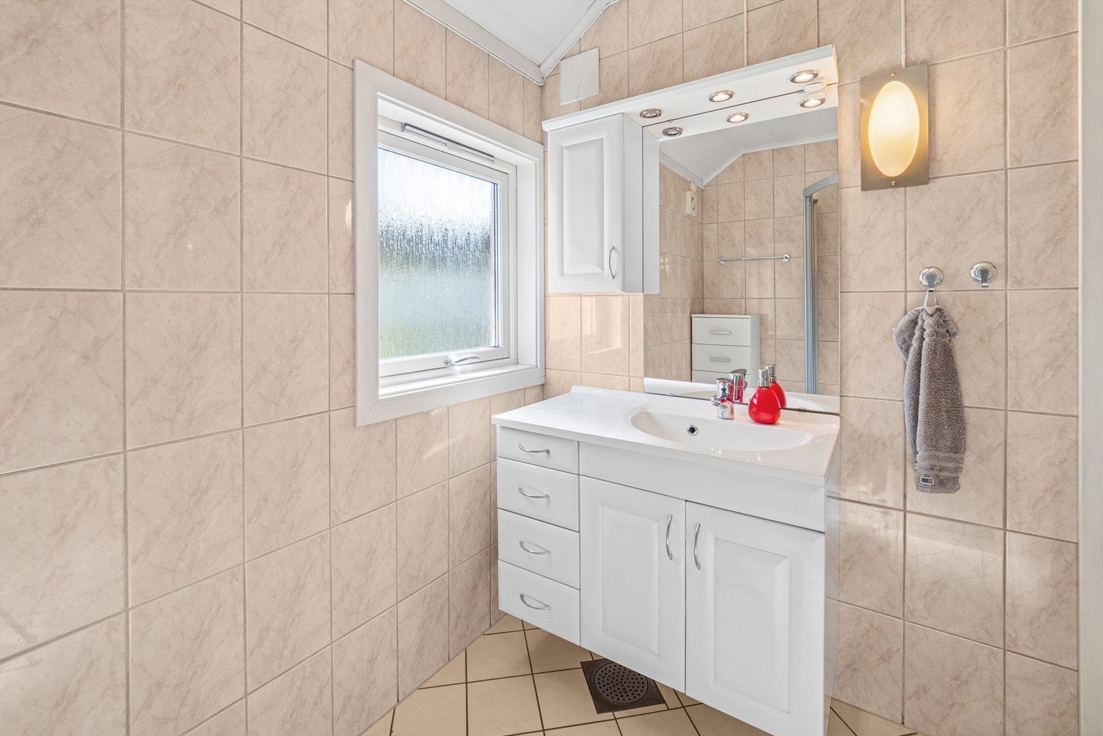 Baderomsinnredningen er pent utført med hvite profilerte fronter, med skuffer og skap, og heldekkende servantplate. Galleribilde