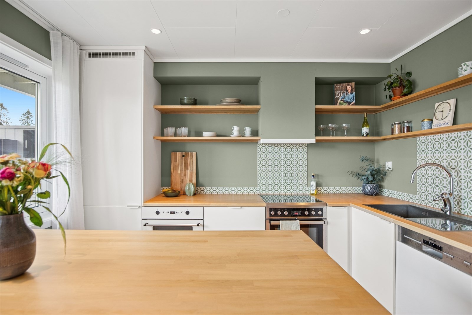 Kjøkkeninnredningen har hvite glatte fronter og flotte fliser over deler av kjøkkenbenken. Galleribilde