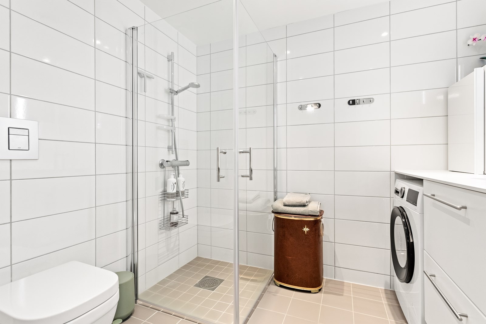 Badet har også kvit og tidlaus innreiing med nedfelt servant i innreiing, spegel med lyslist, dusjhjørne med glasdører og vegghengt toalett. Galleribilde