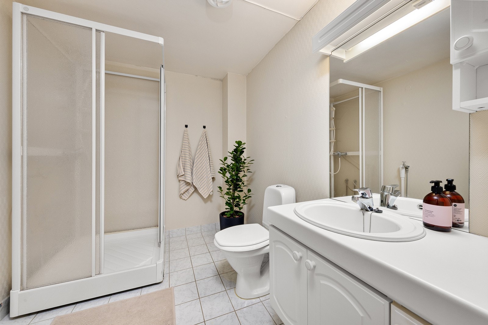 Badet har et flislagt gulv med elektrisk gulvvarme, og rommet er utstyrt med dusjkabinett, toalett og en innredning med nedfelt servant. Galleribilde