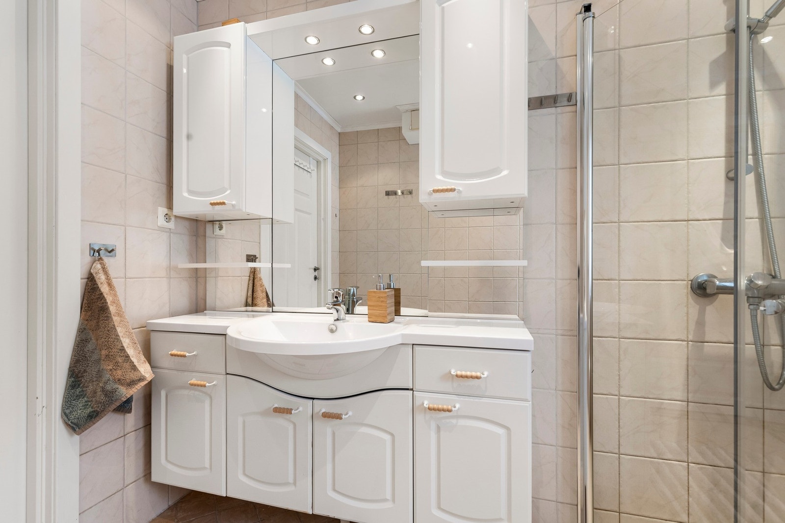 Badet er innredet med en romslig baderomsinnredning med både skap og skuffer, speil med overskap på hver side, dusjnisje med innfellbare glassvegger og vegghengt toalett. Galleribilde