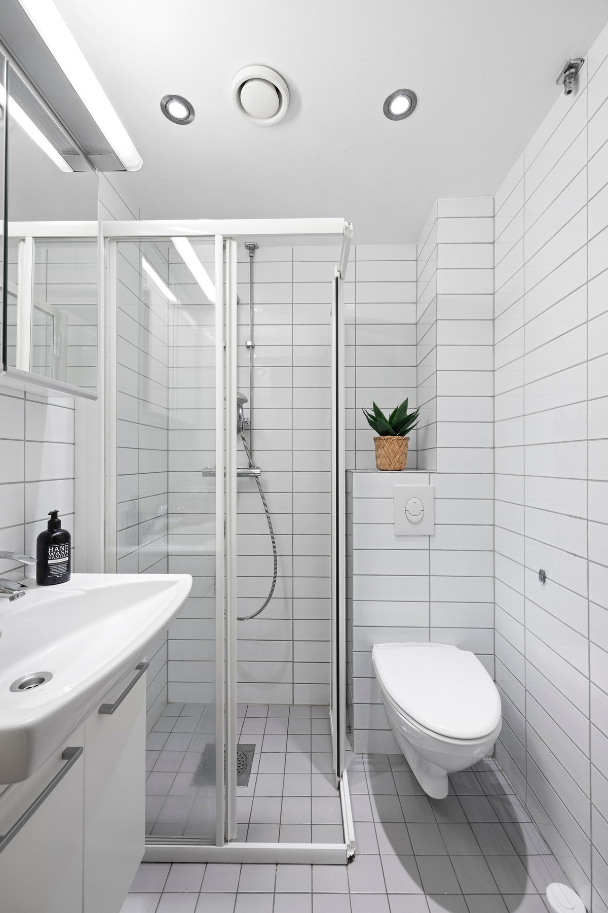 Flislagt baderom med vegghengt wc, servant med underskap, veggskap med speilfronter og dusjhjørne. Galleribilde