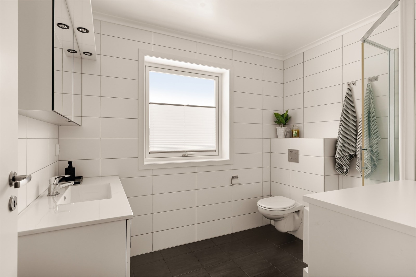 Tidløst flislagt baderom med servant i innredning, vegghengt toalett og dusjkabinett Galleribilde