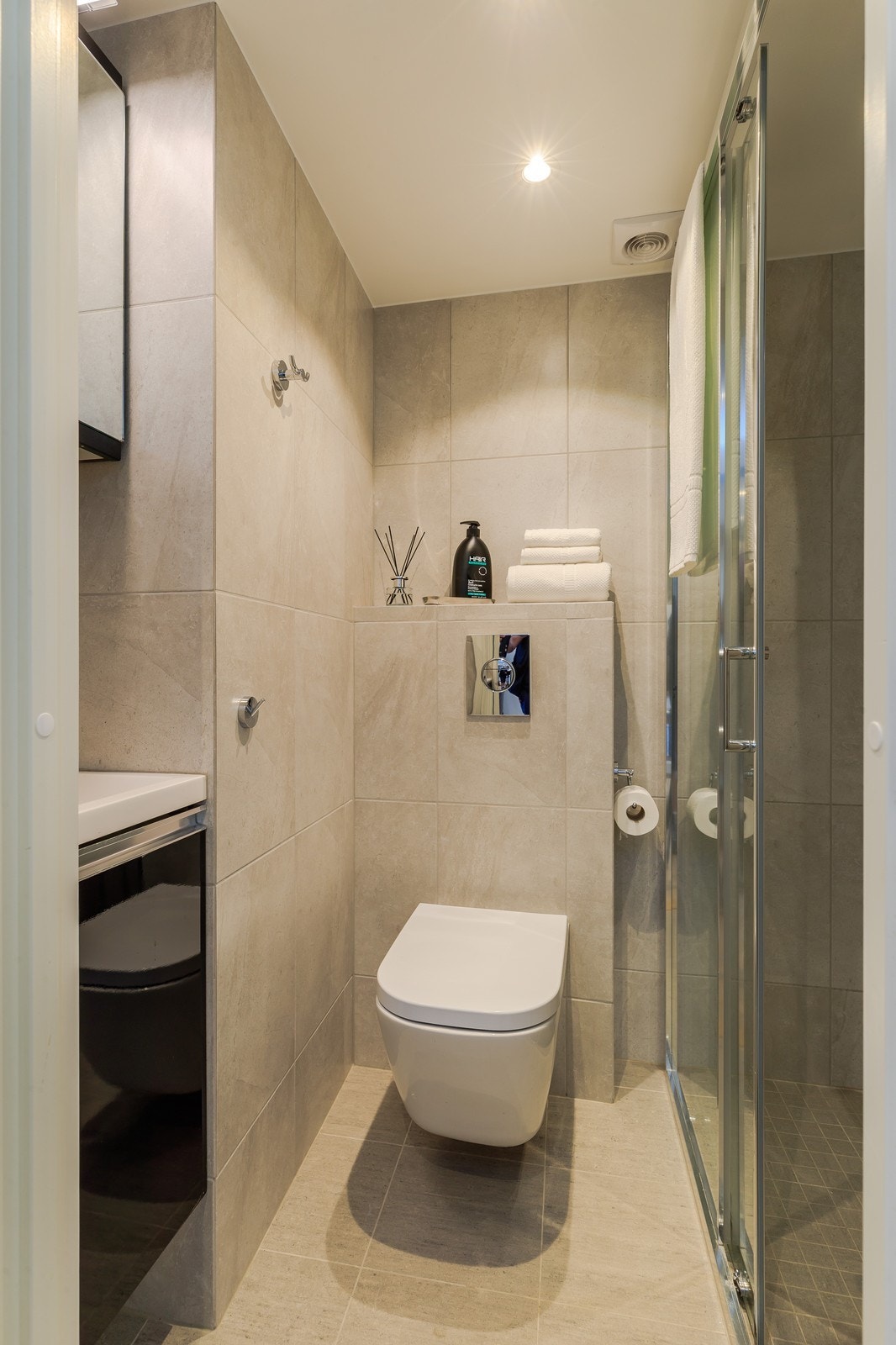 Lekkert flislagt bad med vegghengt toalett, dusjhjørne og servant m/innredning. Galleribilde