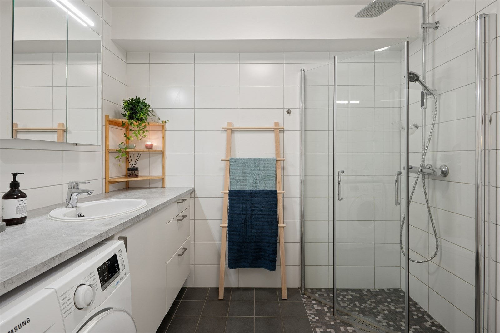 Pent flislagt bad som er innredet med fliser på gulv og vegger, med underliggende varme i gulv. Videre har badet servant nedfelt i benkeplate, servantskuffer, servantskap og opplegg for vaskemaskin Galleribilde