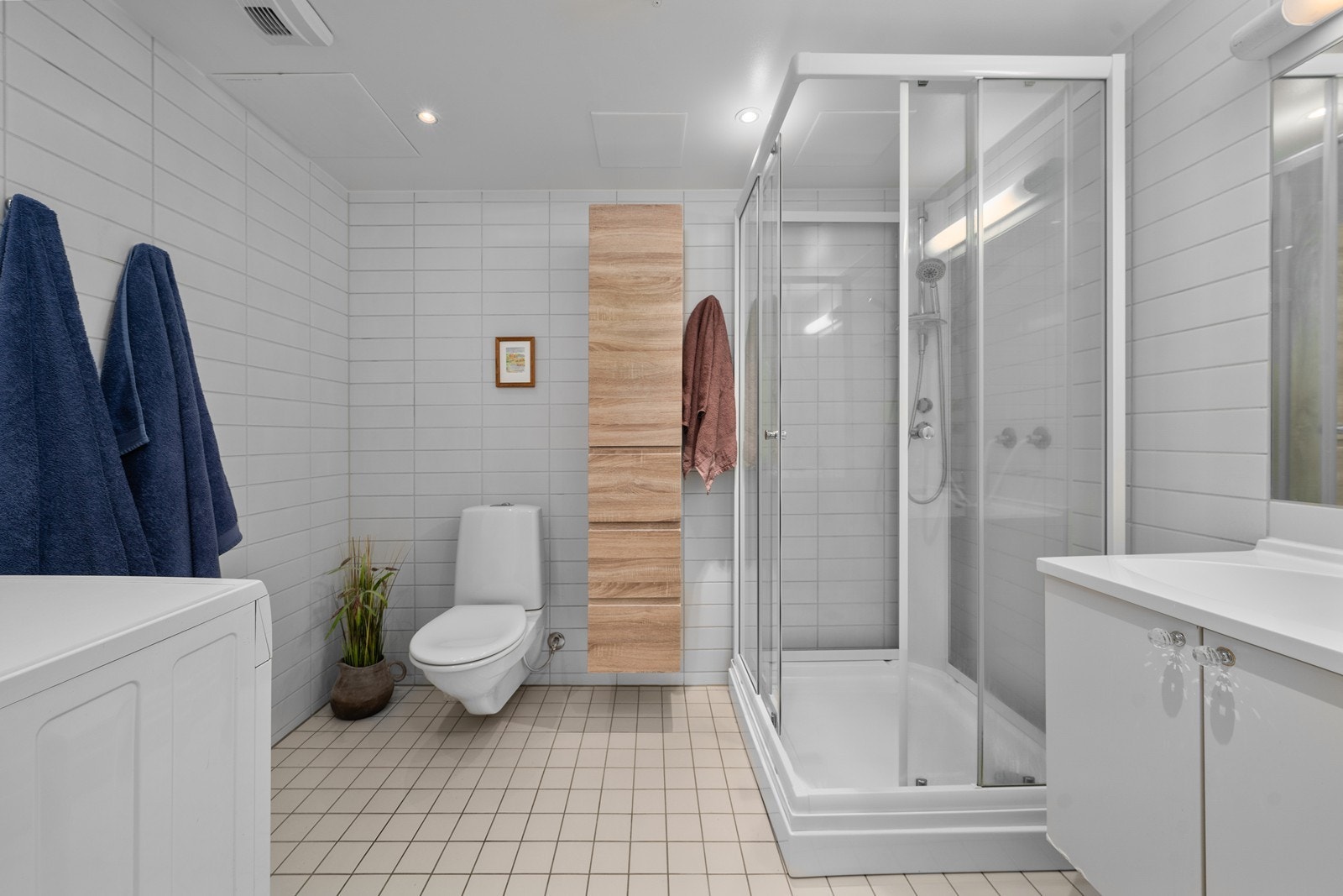 Romslig, helfliset bad med dusjkabinett og praktisk opplegg for vaskemaskin. Galleribilde