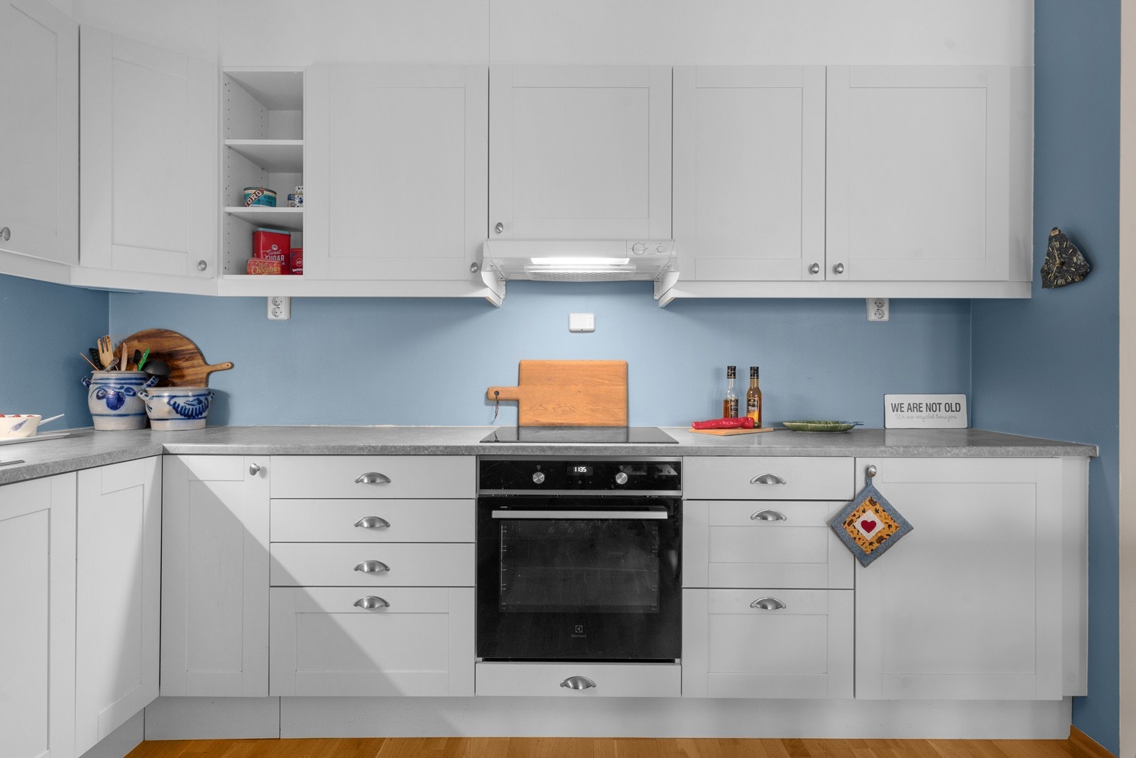 Kjøkkeninnredning med hvite, profilerte fronter, laminatbenkeplate og integrerte hvitevarer. Galleribilde