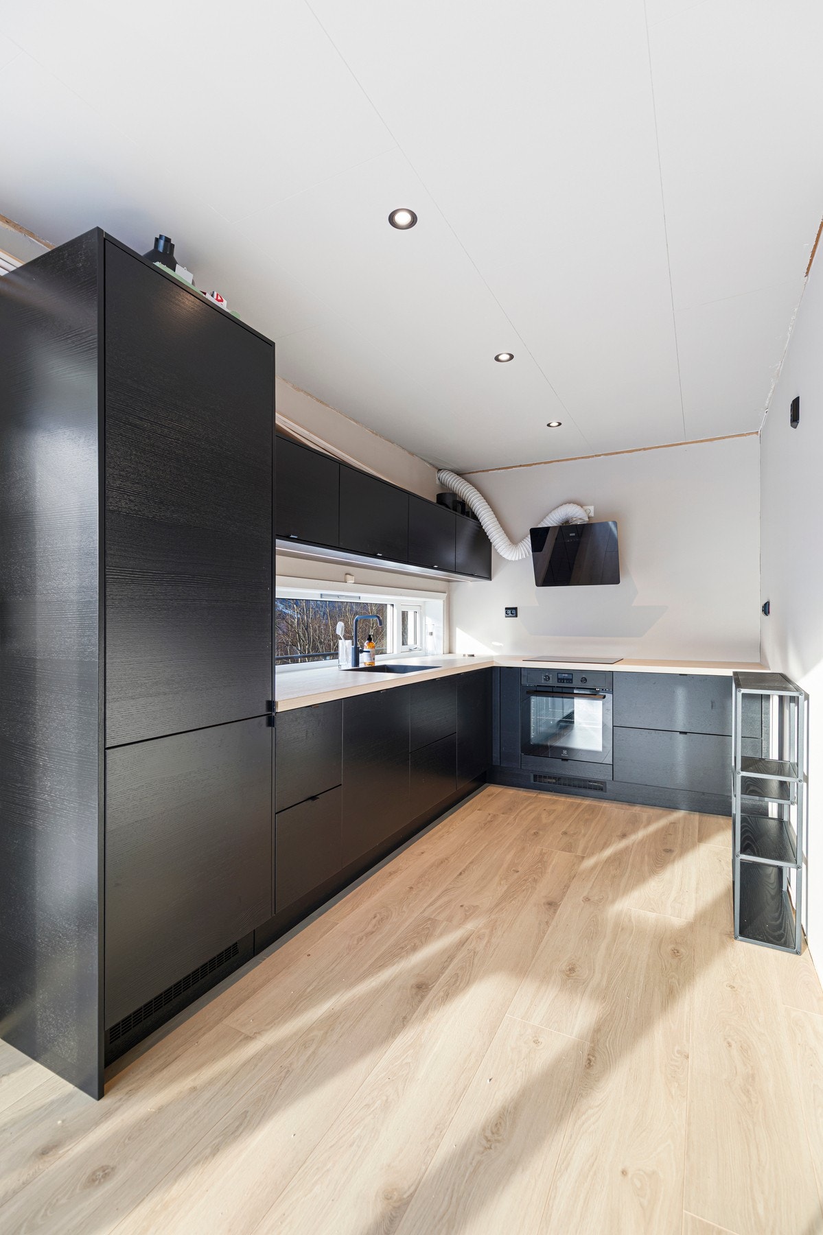 Innredningen har sorte fronter, laminat benkeplate, ventilator og integrerte hvitevarer; stekeovn, platetopp, oppvaskmaskin og kjøleskap med frysedel. Galleribilde