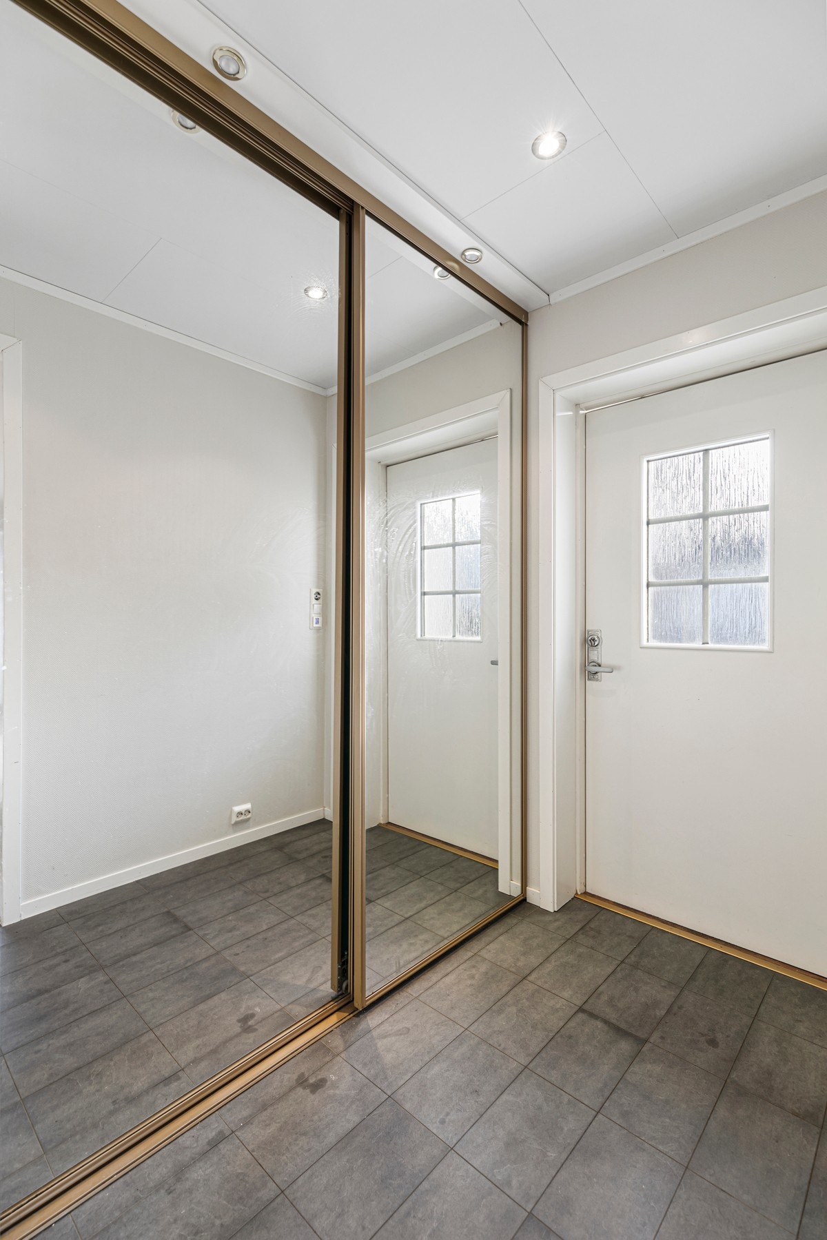 Entre har flislaminat på gulv og tilhørende skyvedørsgarderobe med speilfronter. Galleribilde