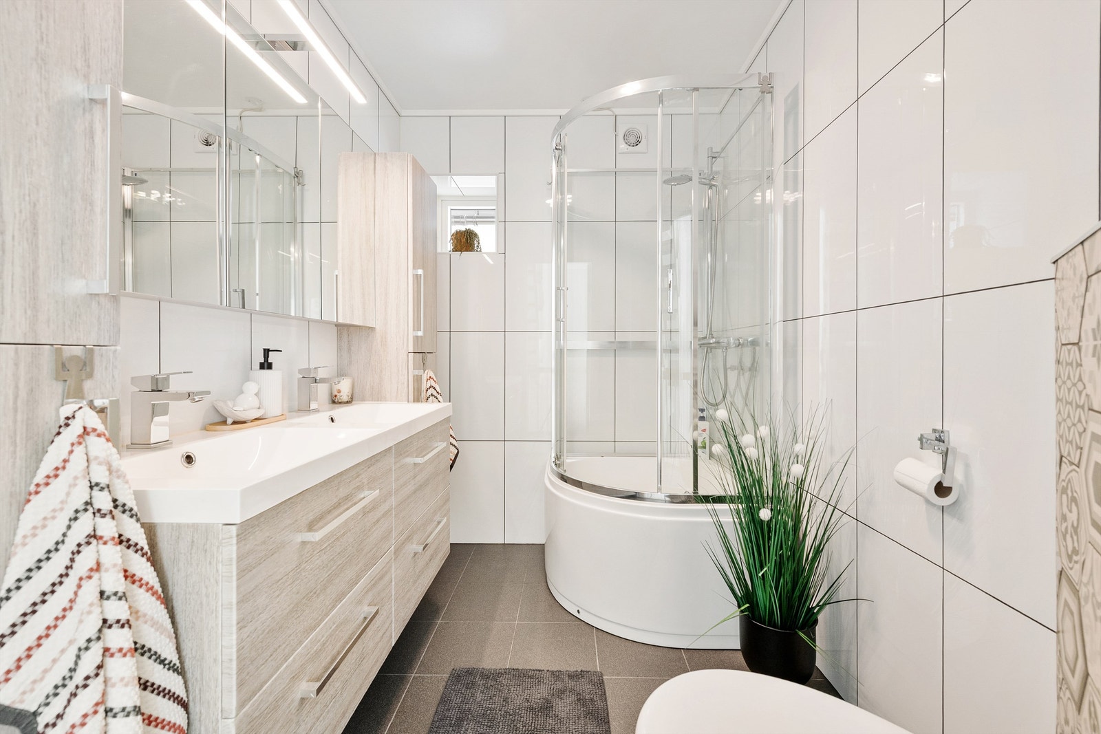 Badet har dusjkabinett med dusjarmatur. Vegghengt toalett. Mekanisk avtrekk med ventil i vegg. Galleribilde