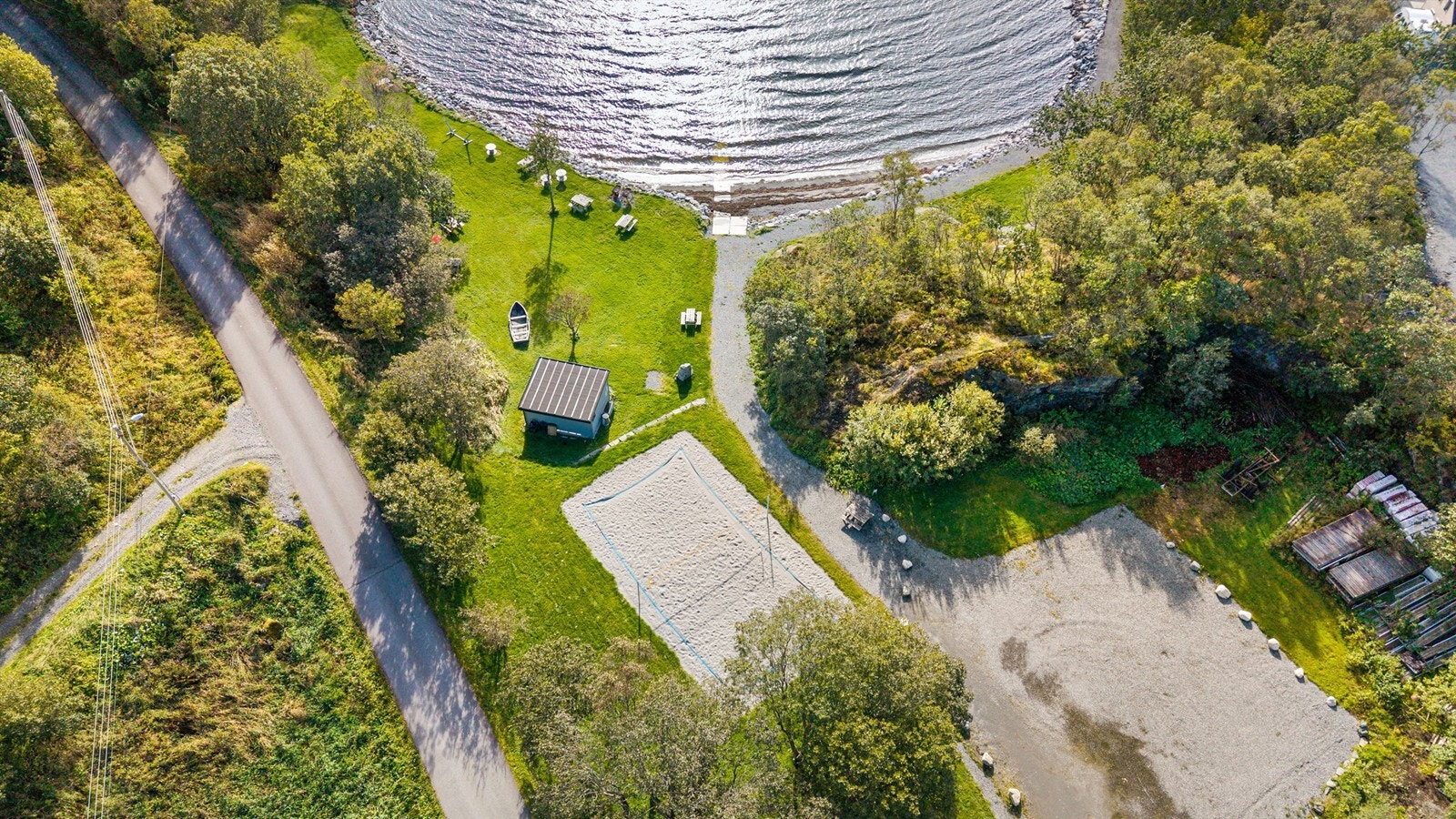 Dronebilde av friområdet tatt fra fugleperspektiv som viser parkering, sandvolleyballbane, grillplass og flotte bademuligheter Galleribilde
