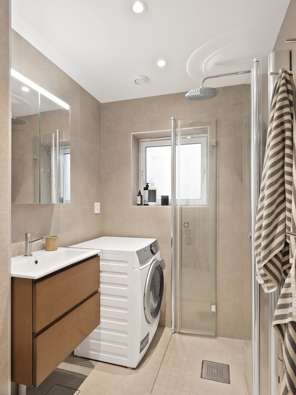 Flislagt bad med dusjhjørne, vegghengt toalett og opplegg for vaskemaskin. Galleribilde