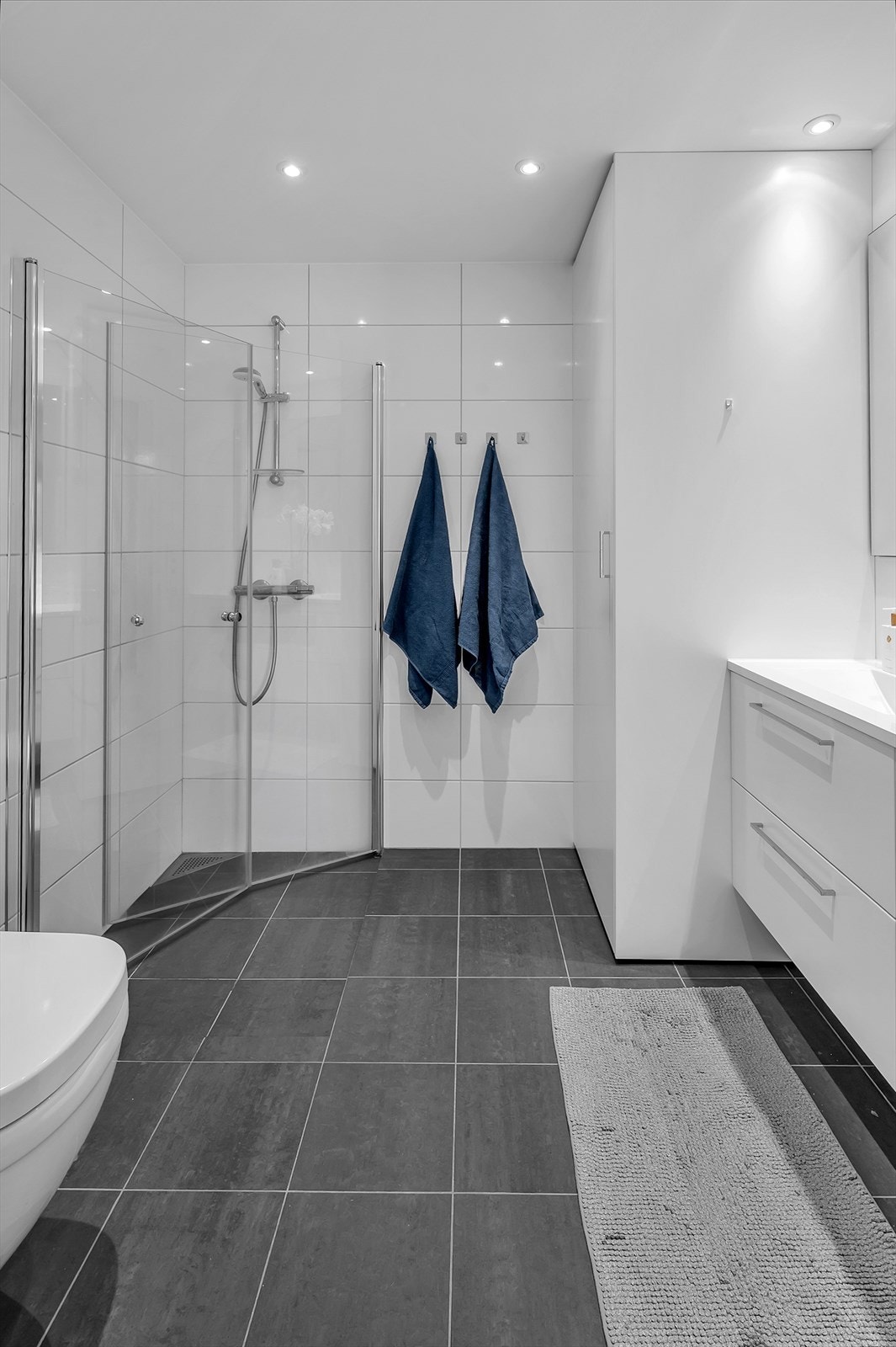 Bad/vaskerom med nedfelt servant, veggmontert toalett, dusjvegger/hjørne og opplegg for vaskemaskin. Galleribilde