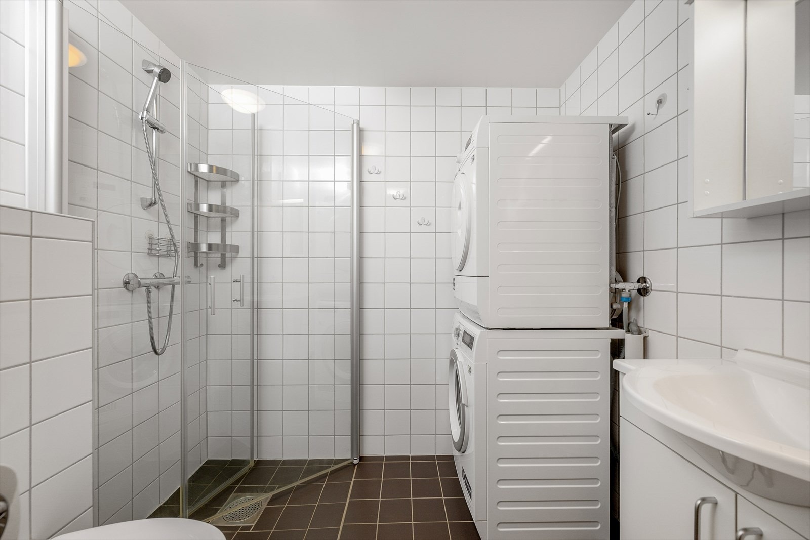 Flislagt bad med dusjhjørne og praktisk opplegg for vask- og tørkemaskin. Galleribilde