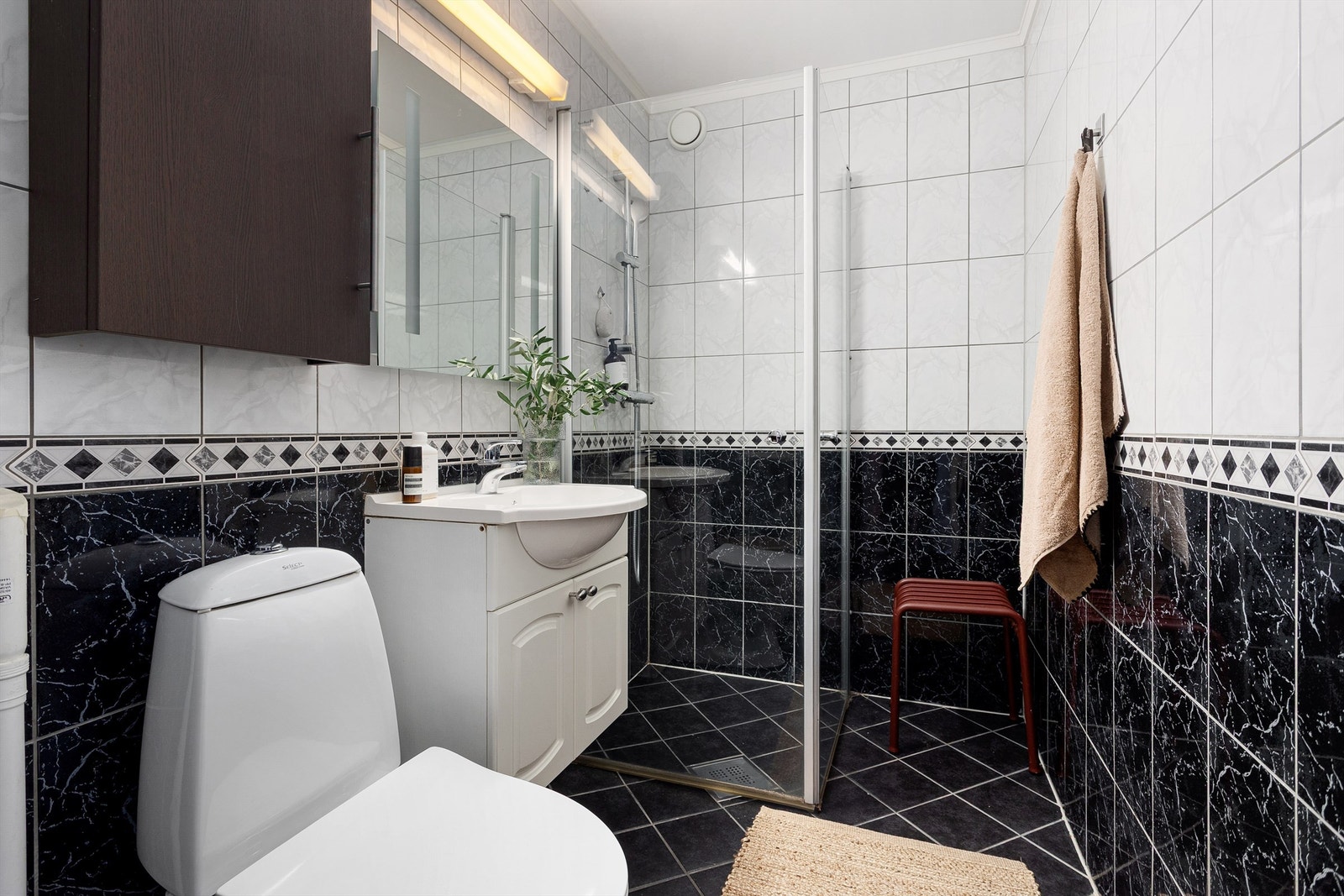 Rommet er innredet med klosett, servant med tilhørende innredning, speil med belysning samt dusjhjørne med svingbare glassdører. Galleribilde