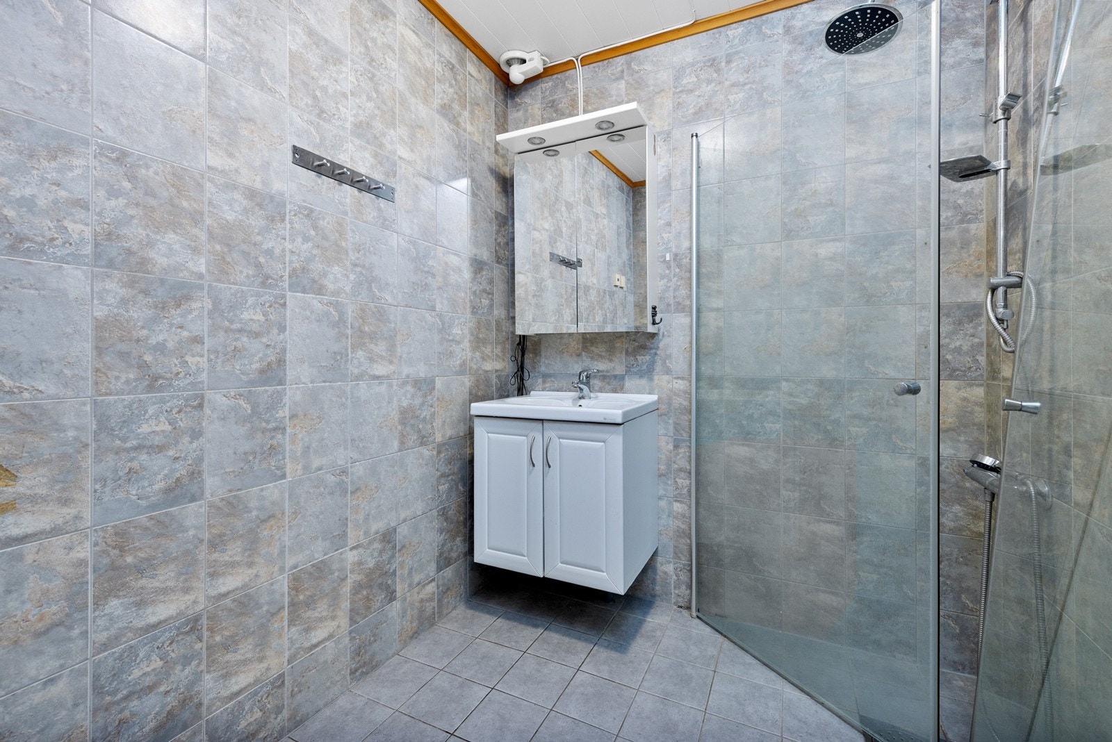 Badet er flislagt og har elektrisk gulvvarme. Rommet er utstyrt med servantinnredning med overskap, dusjhjørne med glassdører, samt opplegg for vaskemaskin. Galleribilde