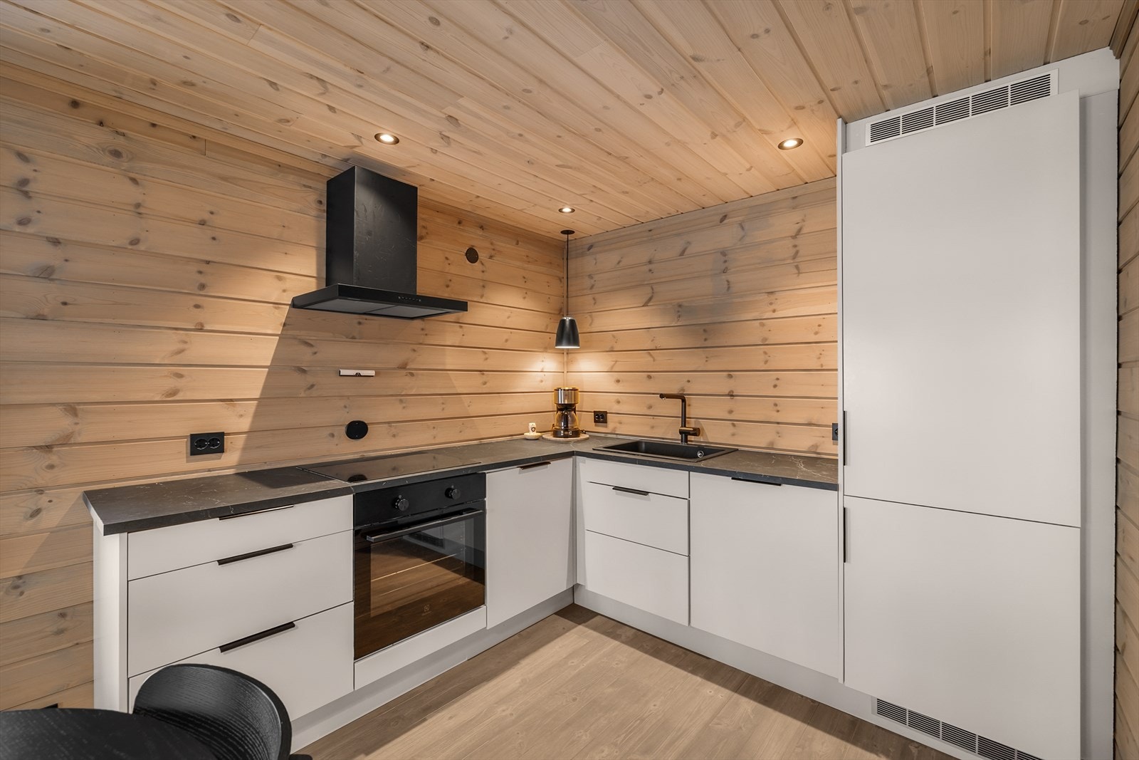 Pent kjøkken innredet med glatte overflater, utstyrt med integrert platetopp, stekeovn, oppvaskmasking og kjøl/fryseskap. Kjøkkenventilator med mekanisk avtrekk ut samt vannstoppsystem og komfyrvakt Galleribilde