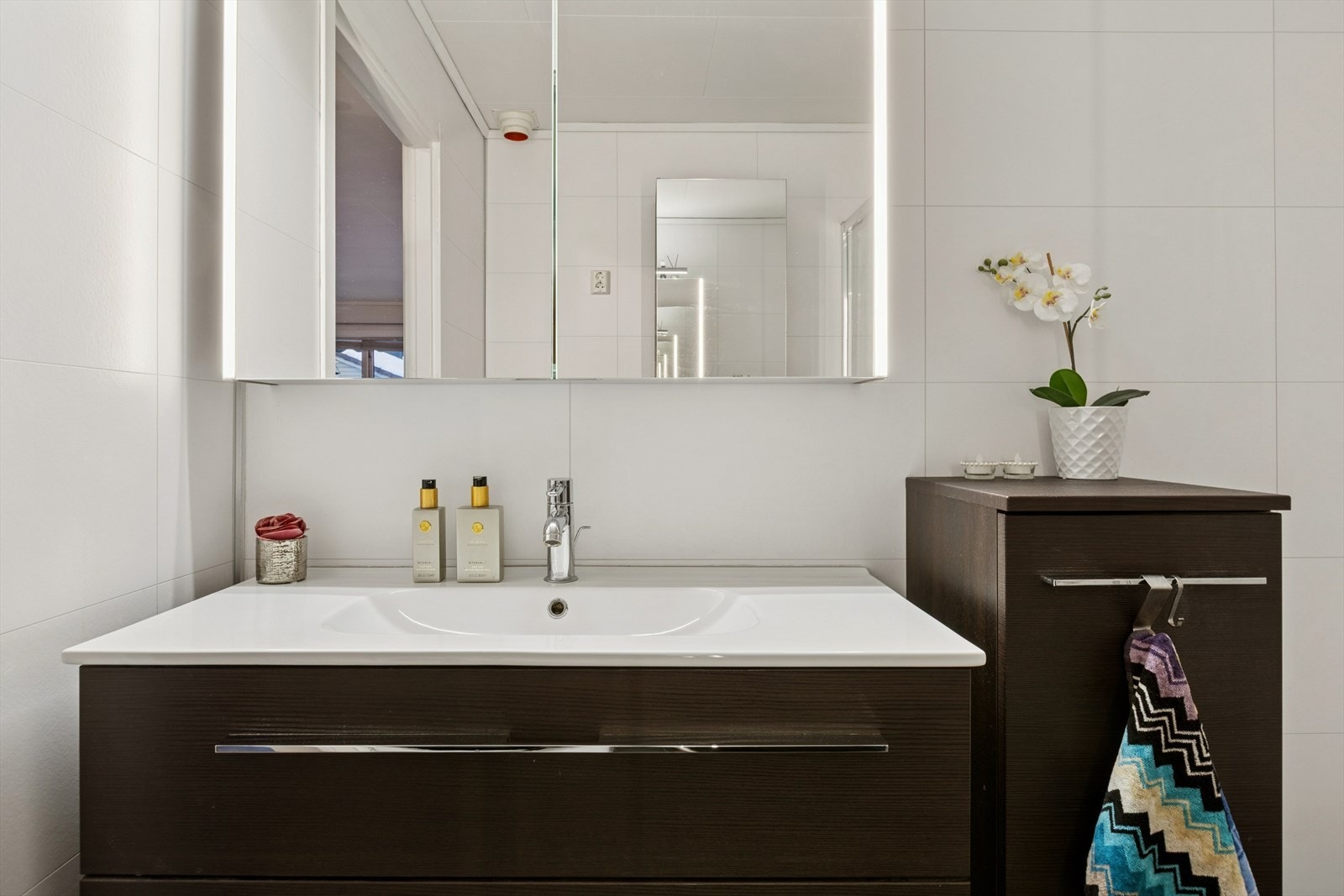 Badet er innredet med et toalett, et dusjhjørne med skyvedører, en baderomsinnredning med servant og ett-greps blandebatteri, samt speilskap. Galleribilde