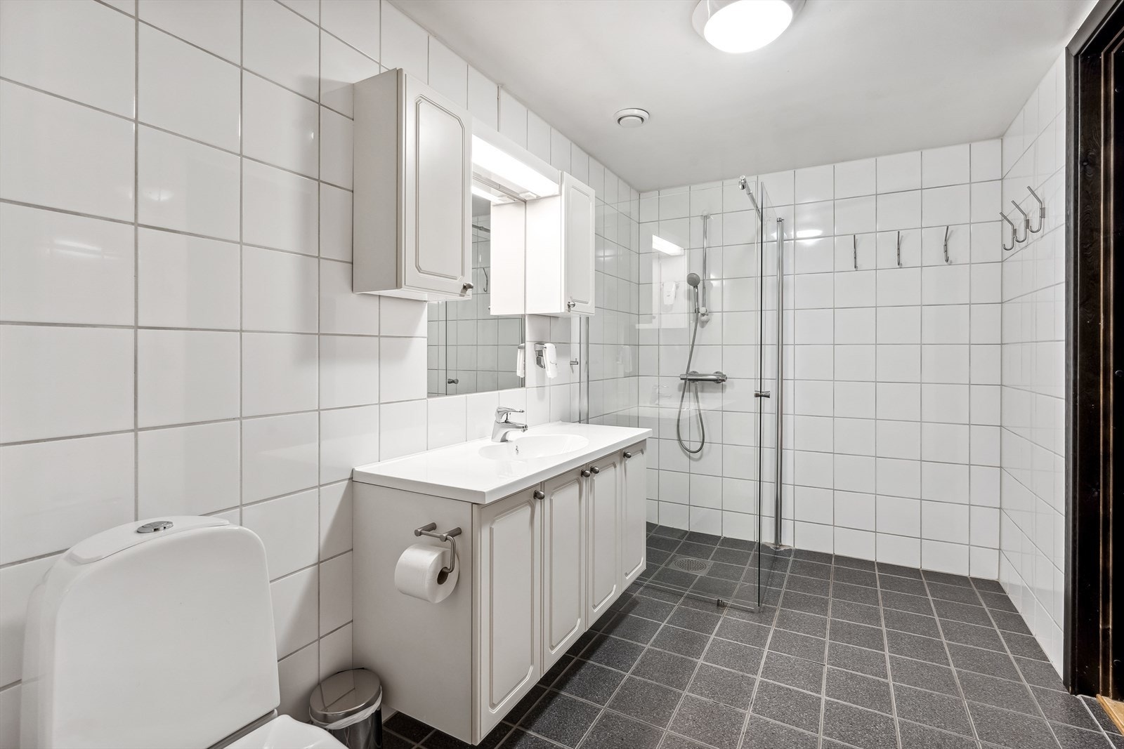 Badet er innredet med vegghengt servantinnredning, vegg skap og speil med lys. Dusjhjørne med glassvegger. Galleribilde