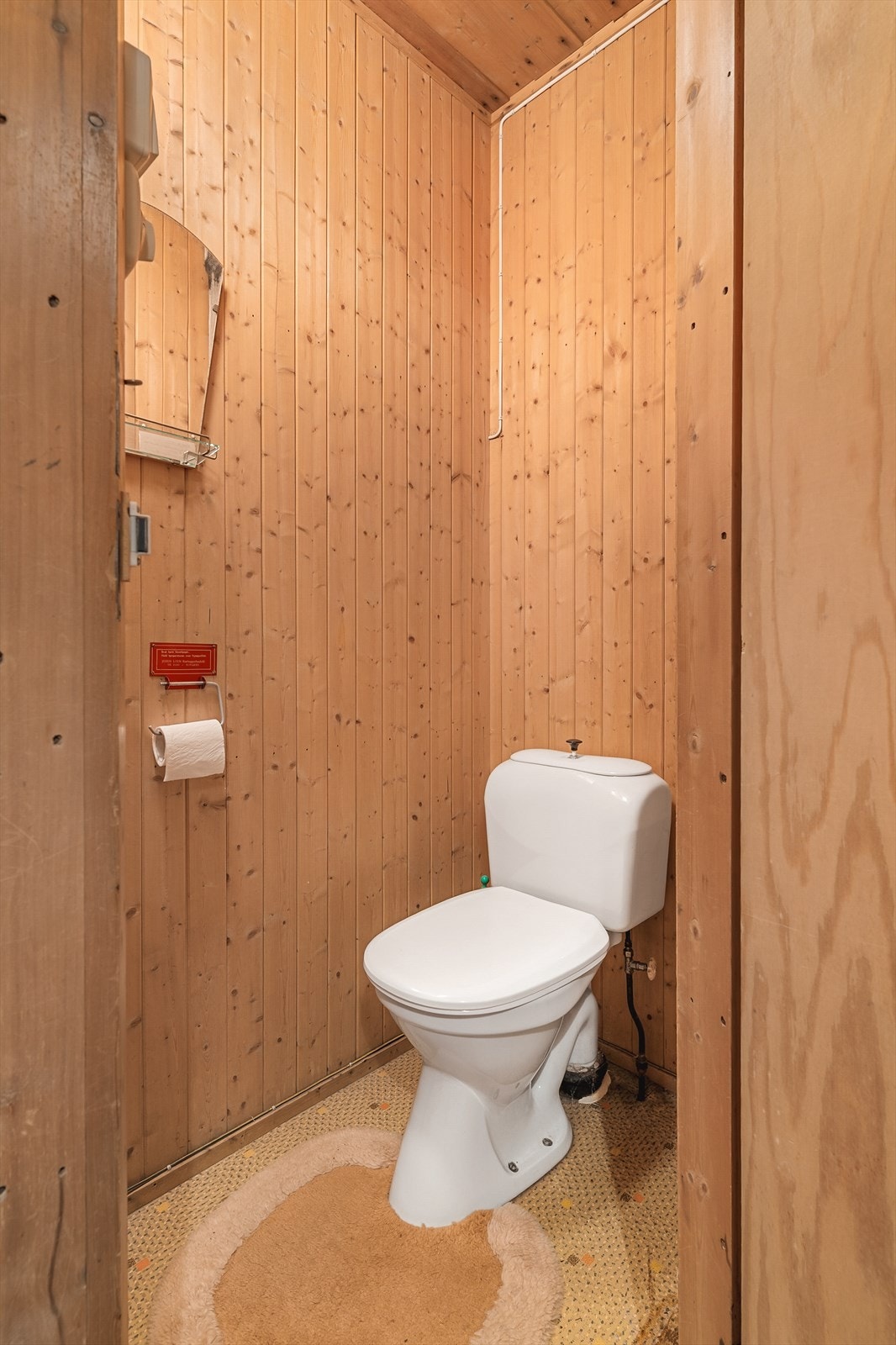 Praktisk toalettrom i hovedetasjen med gulvmontert WC og trepanel på vegger. Galleribilde