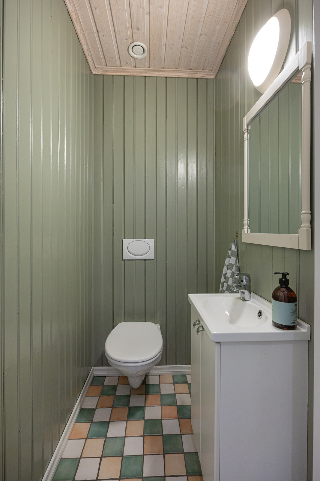 Wc-rommet i 1. etasje har vegghengt toalett, grønne panelvegger og fine gulvfliser i ulike farger Galleribilde