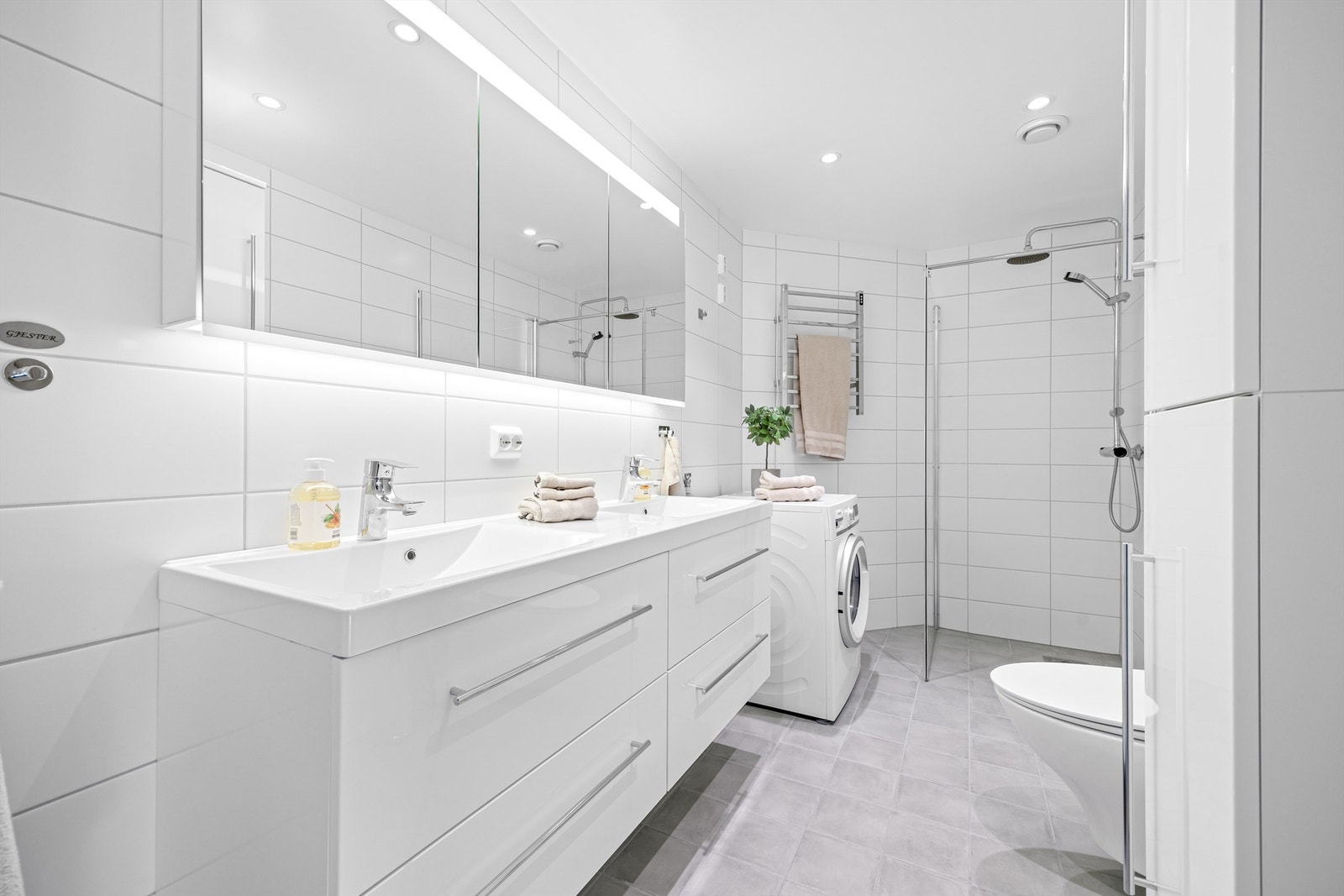 Innbydende og romslig bad med dobbelt servantinnredning, dusjhjørne, toalett og opplegg til vaskemaskin. Galleribilde