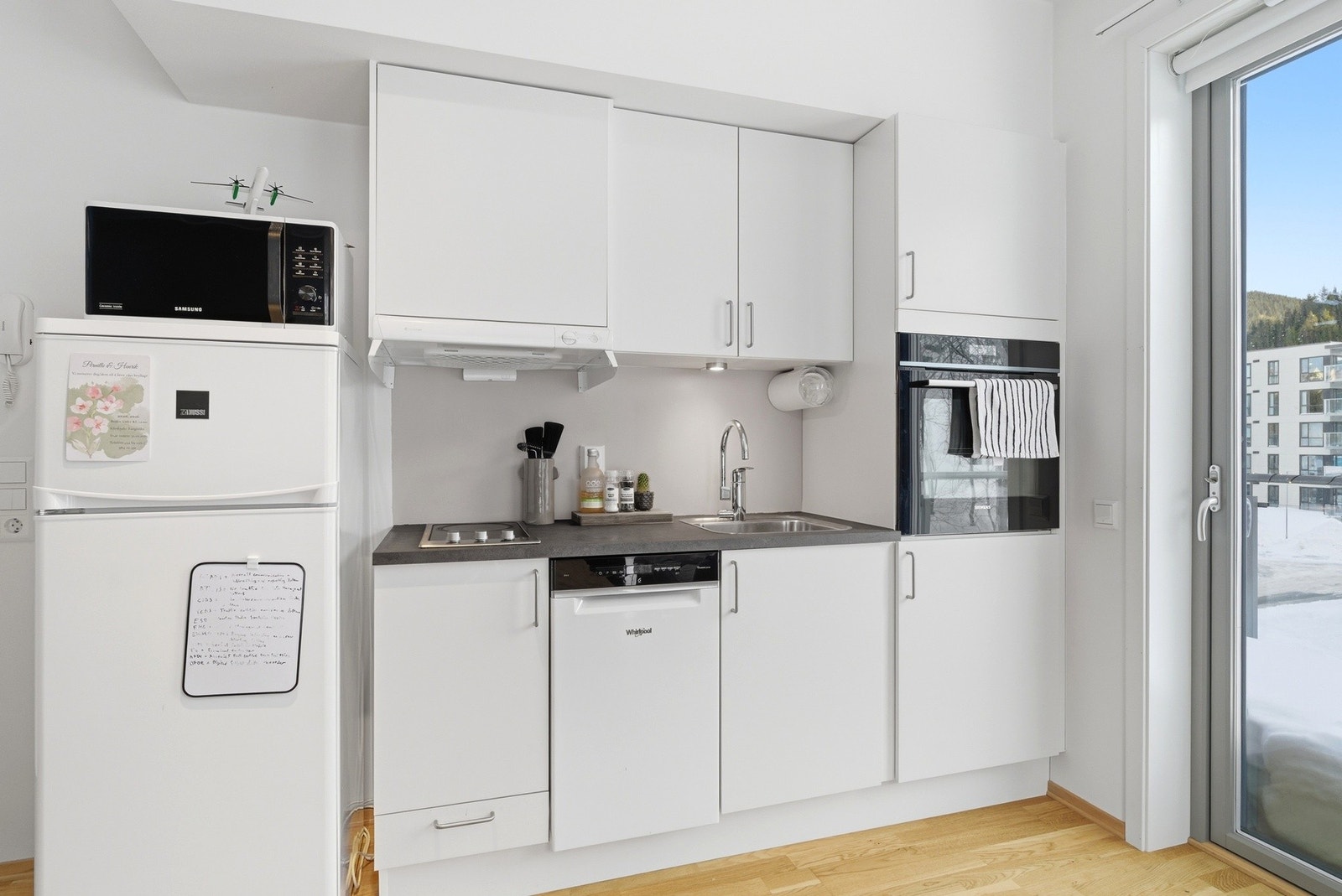 Praktisk kjøkken med høyskap, integrert stekeovn, overskap og benkeinnredning - Hvite, slette fronter. Galleribilde