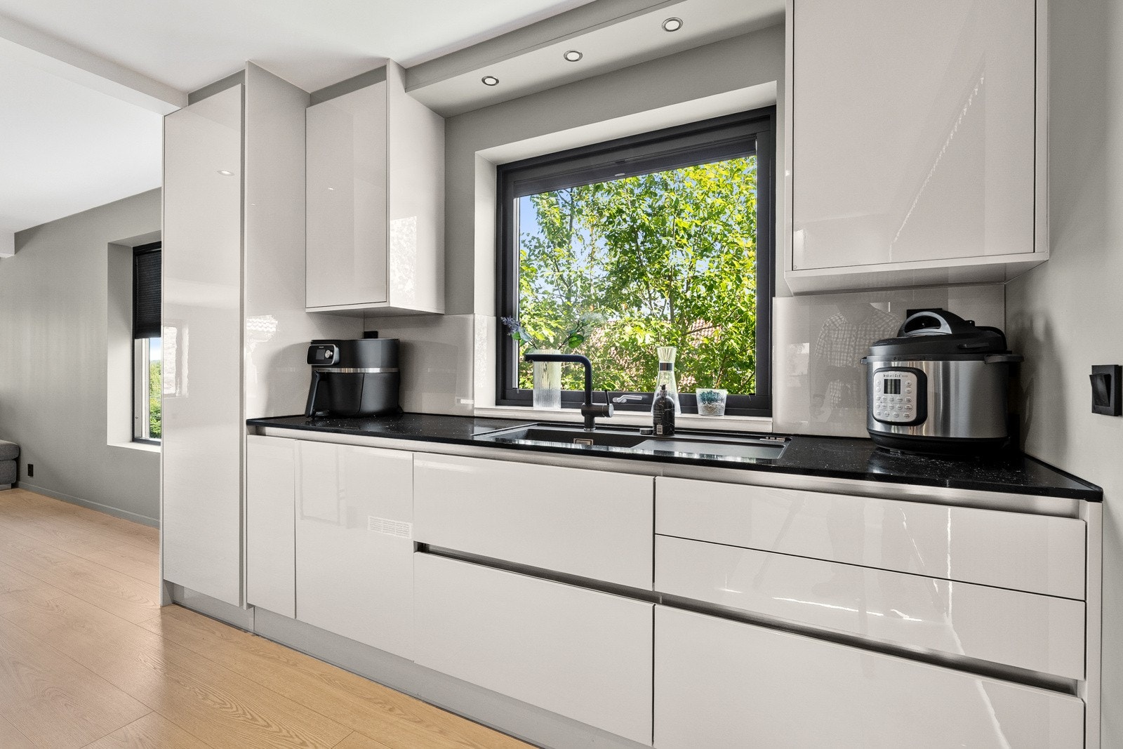 Kjøkken fra 2021 med glatte fronter, integrerte løsninger og stilfull benkeplate i stein. Store vinduer gir godt lysinnslipp og en hyggelig arbeidsplass ved kjøkkenbenken. Galleribilde