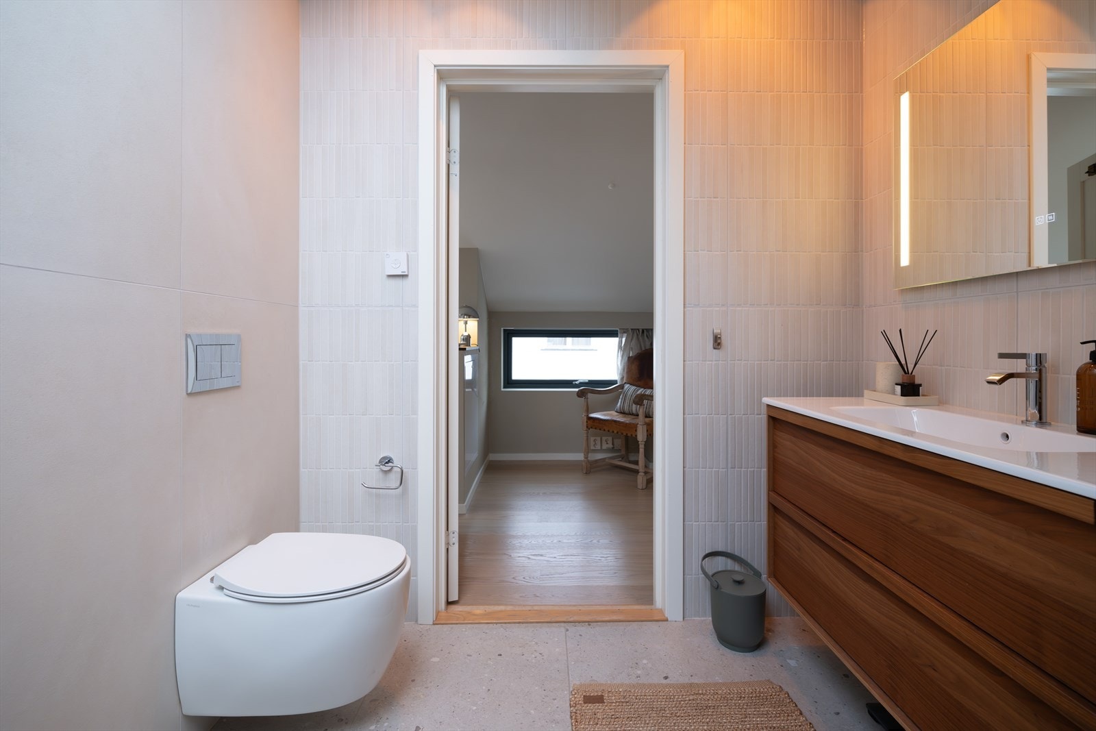 Baderommet har flislagte overflater kombinert med sparklet og malte plater og innredningen består av benkeskap med glatte fronter og speil over servant Galleribilde