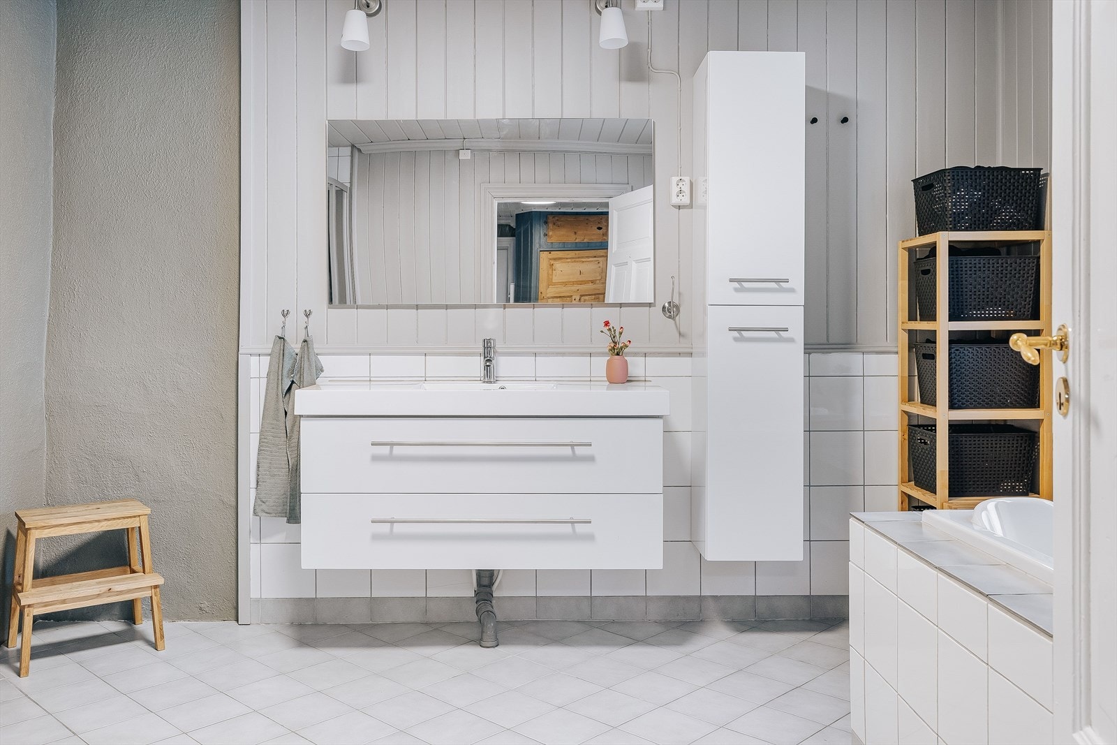 Moderne baderomsinnredning med skuffer og heldekkende servant, speil med belysning over, samt ekstra vegghengt høyskap ved siden av. Galleribilde