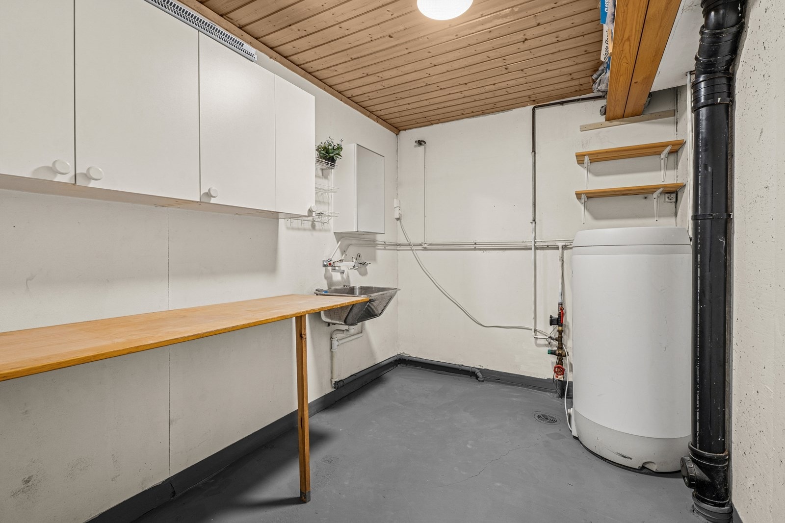 Separat vaskerom innredet med bl.a. skap, hyller og en praktisk benk for arbeidsplass. Vaskekum i stål og varmtvannsbereder. Galleribilde