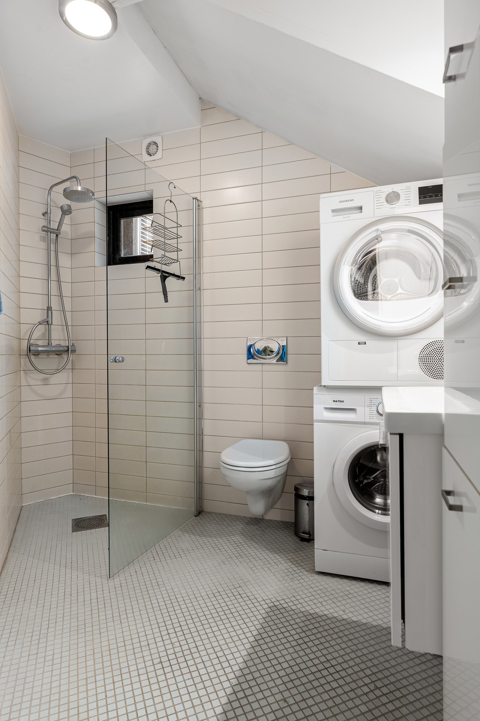 Bad med dusjhjørne, vegghengt wc og opplegg for vaskemaskin.