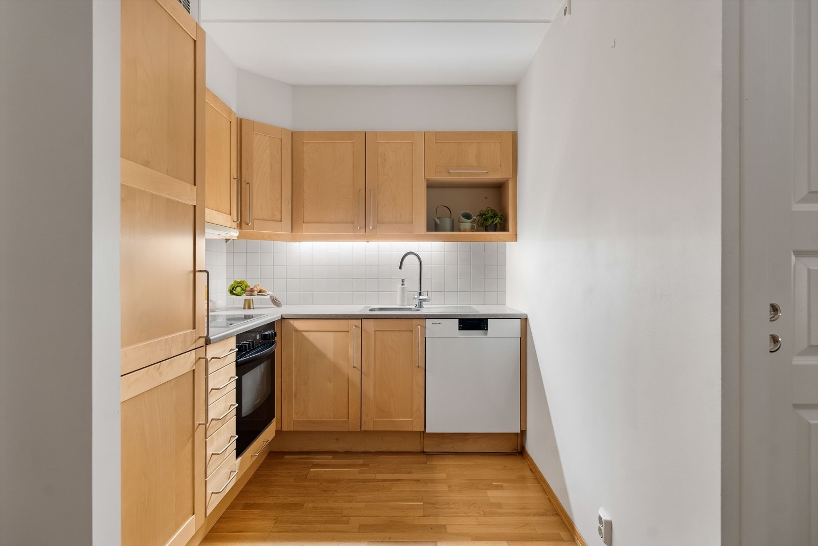 Innredningen har profilerte fronter, nedfelt oppvaskkum og lysegrå benkeplate av laminat. Over benken er det belysning, og over kokesonen er en ventilator etablert med avtrekk. Galleribilde