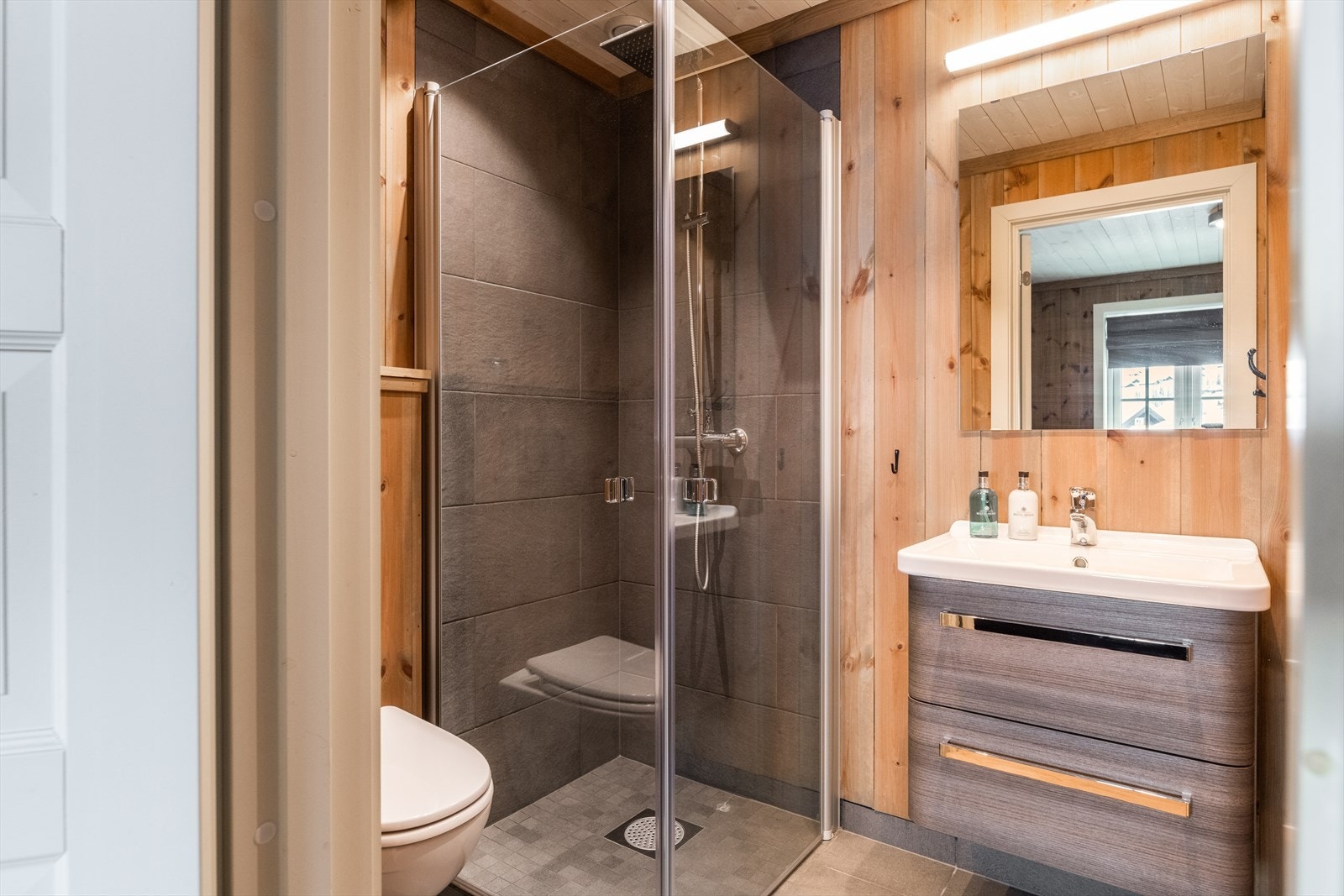 Badet har flis på gulv og i dusjhjørne, ellers panel på vegger. Her er det vegghengt toalett, dusjhjørne med dusjdører og innredning med heldekkende hvit vask, underskuffer med slette fronter og speil. Det er mekanisk ventilasjon. Galleribilde