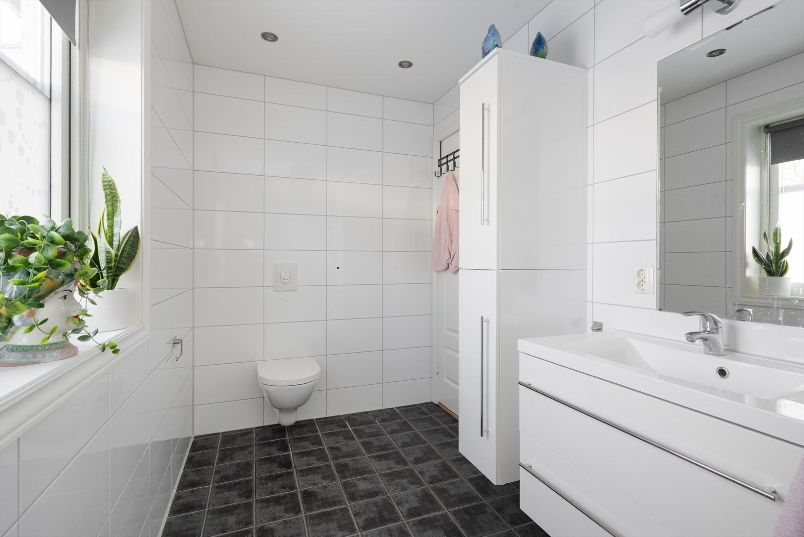 Badet inneholder heldekkende servant med underskap, speil med lys over, veggmontert skap, vegghengt toalett og plassbygget dusjsone. Galleribilde