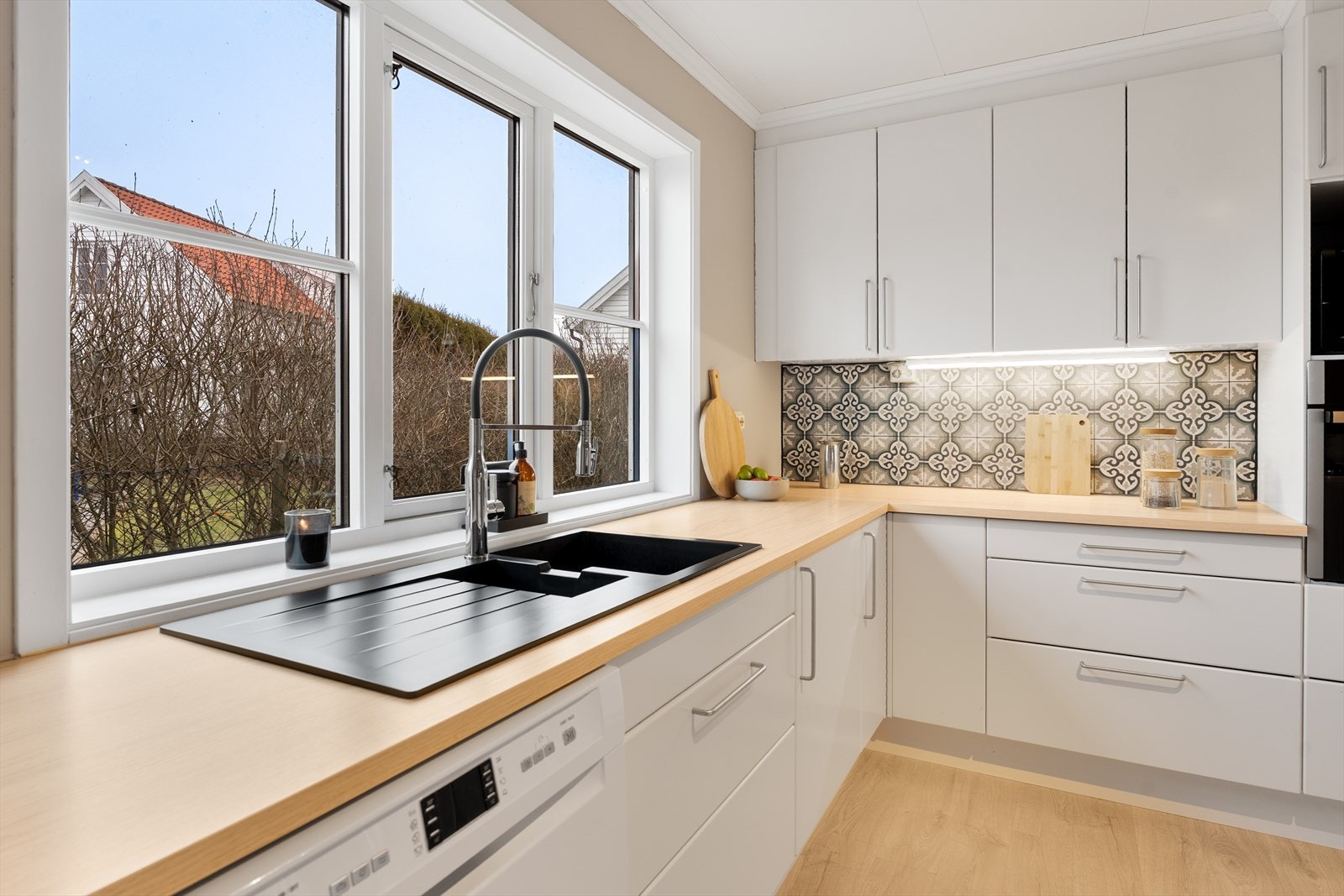 Kjøkken med store vinduer over benkeplaten som gir godt naturlig lys og en lys arbeidsflate. Galleribilde