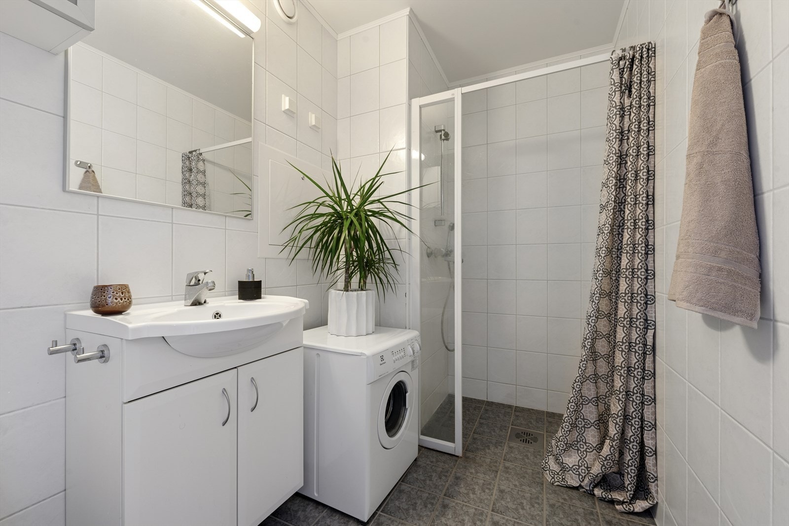 Et tidløst bad med lyse fliser. Her er det opplegg for vaskemaskin og tørketrommel. Galleribilde