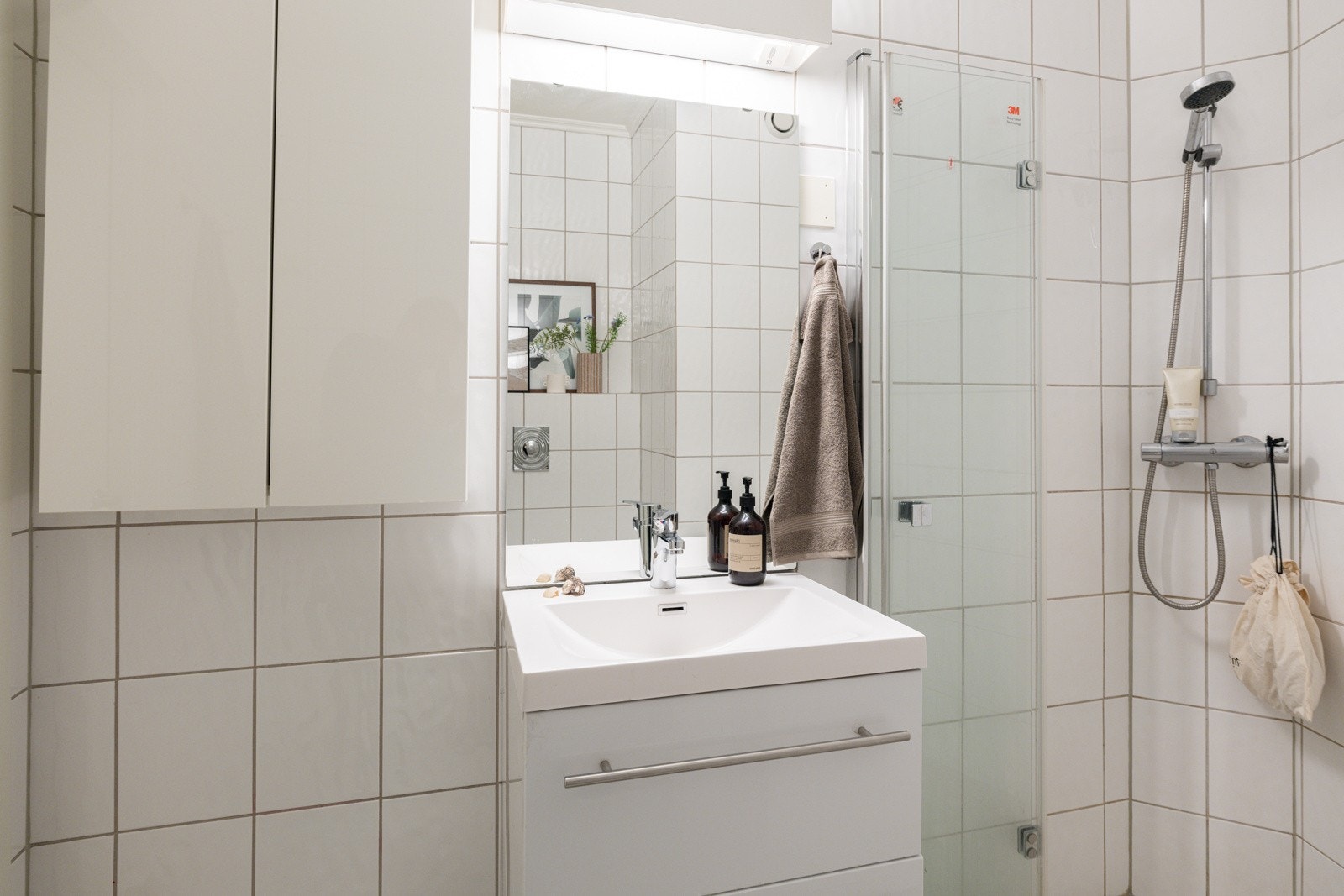 Moderne baderomsinnredning med skuffer og ovenpåliggende servant, speil med belysning over, samt ekstra vegghengt skap ved siden av. Galleribilde